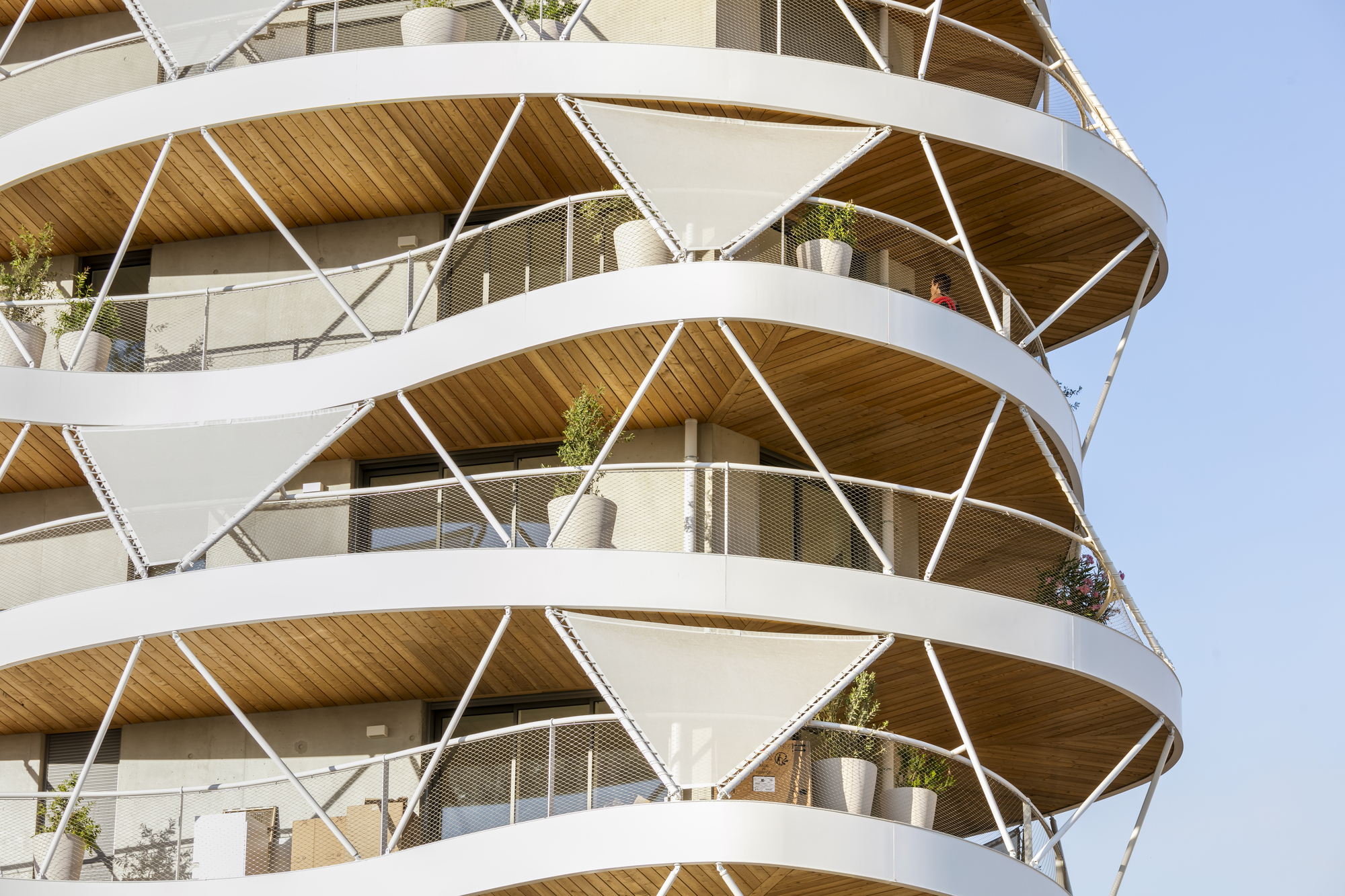 Close-up of the helical balcony structure with timber soffits and white steel bracing carrying potted plants