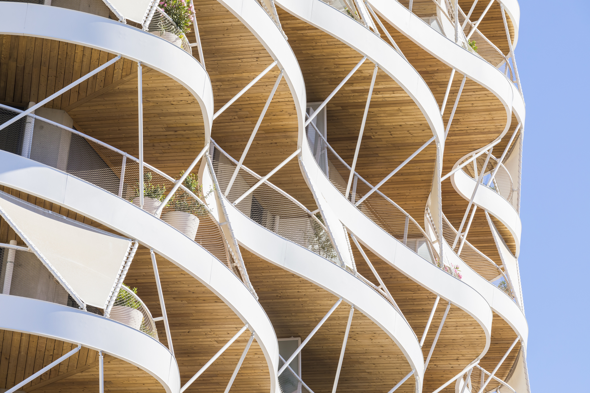 Detail of the criss-crossing white structural exoskeleton wrapping the curved balconies with timber ceilings