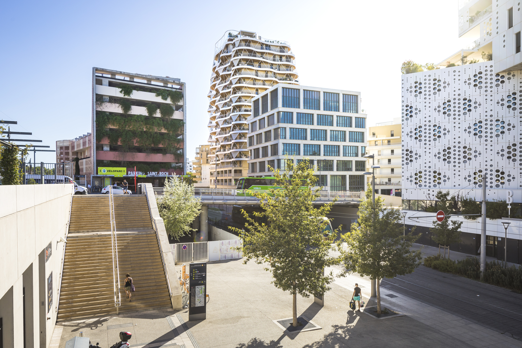 Plaza view with pedestrians and trees showing the tower among neighboring buildings in late afternoon