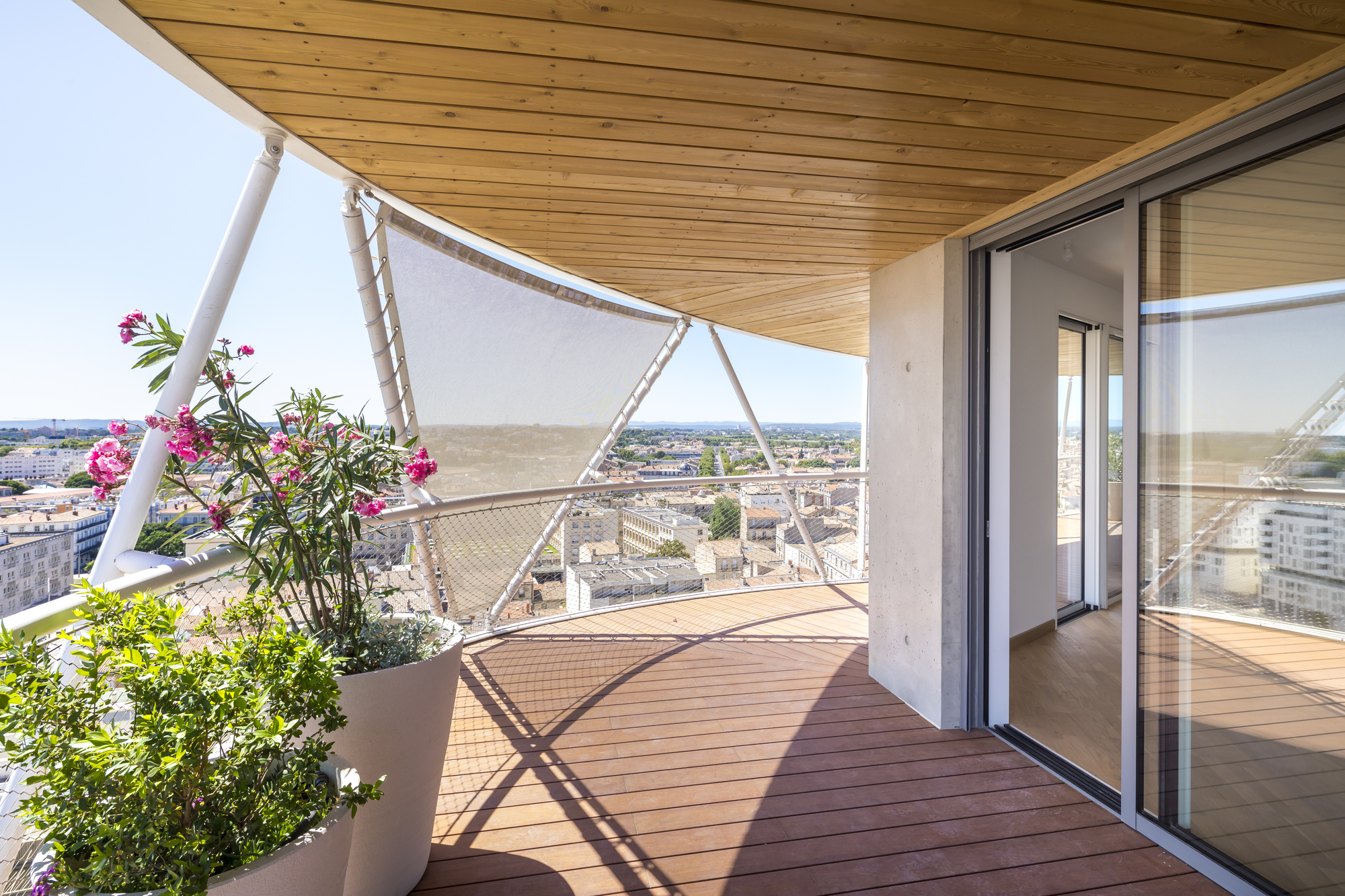Timber-decked balcony with planted pots and tensile fabric shade overlooking the rooftops at dusk