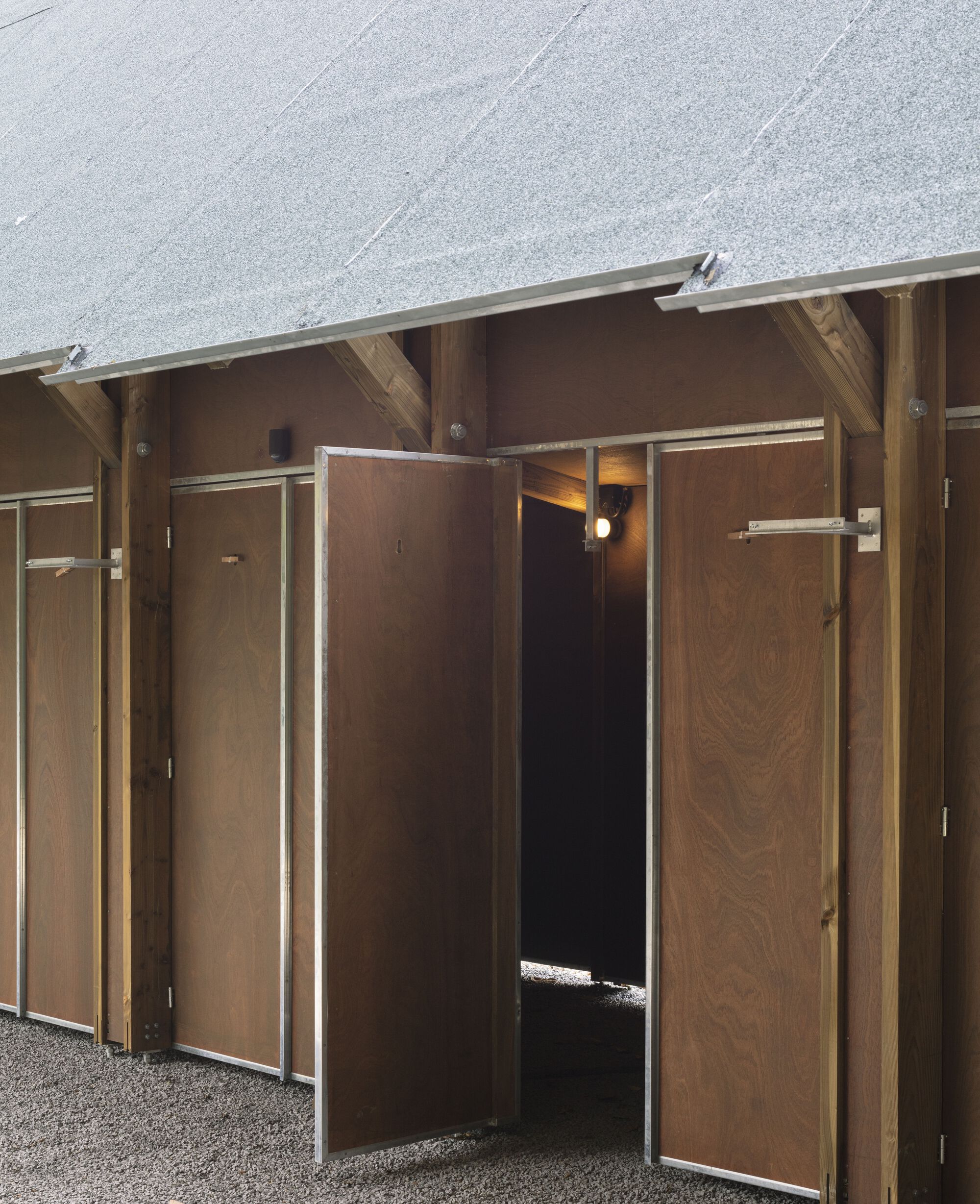 Close-up of timber-framed doorways with plywood panels and metal edging beneath a pitched gravel roof