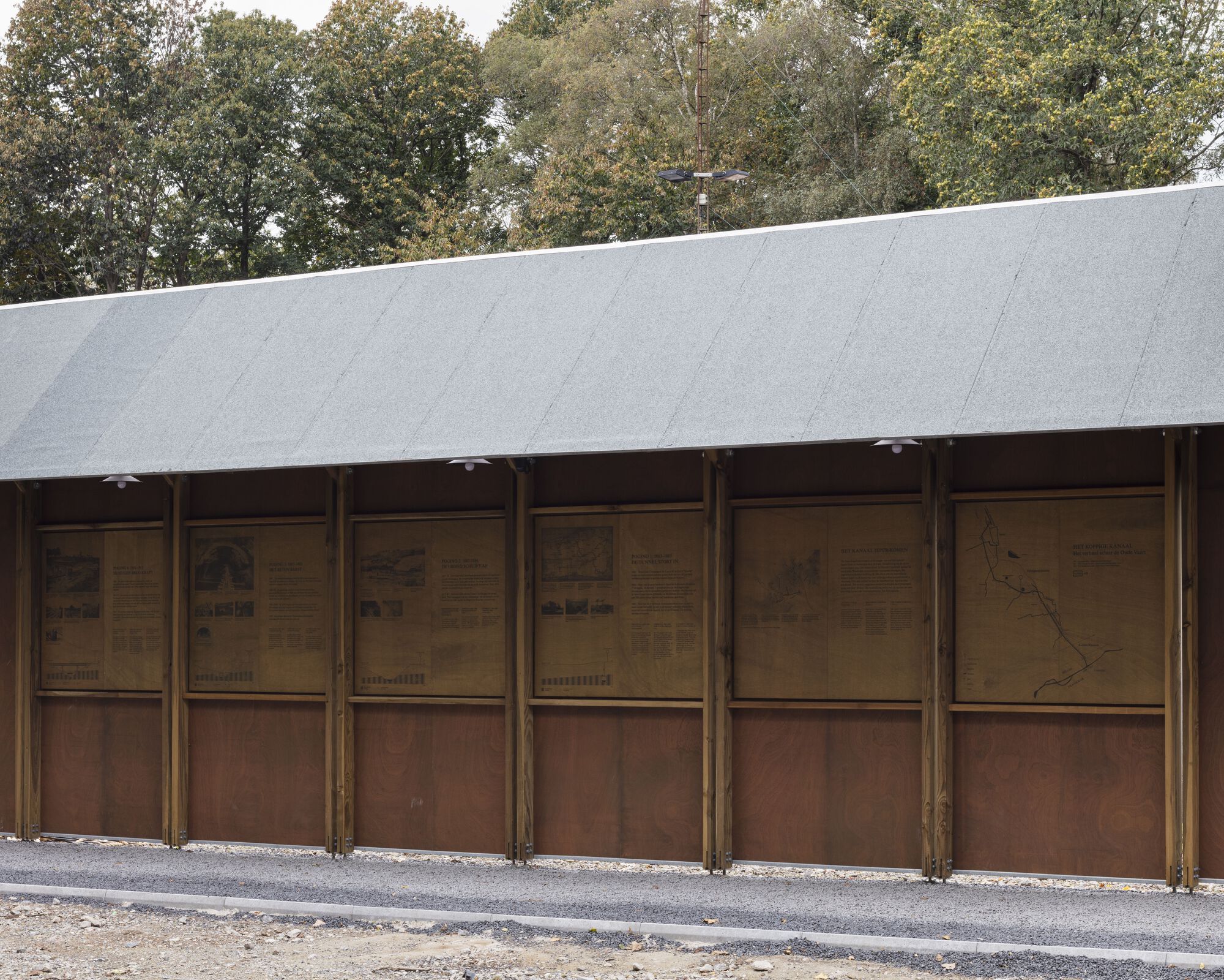 Exterior wall of vertical timber framing with corten-clad lower panels beneath a sloping metal roof