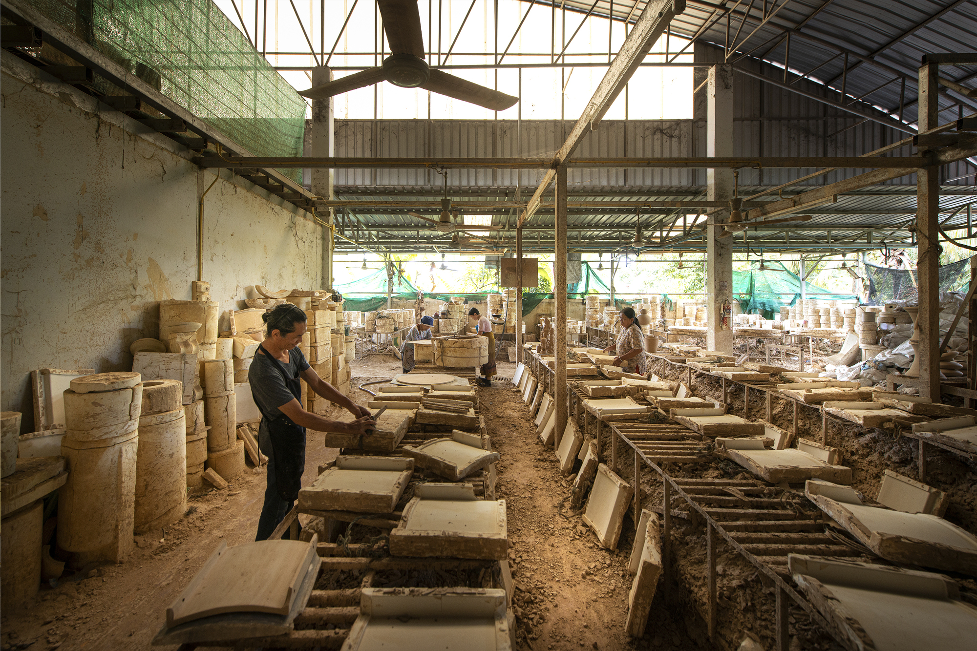 Interior of ceramics workshop with workers forming clay pieces under the skylit steel truss roof
