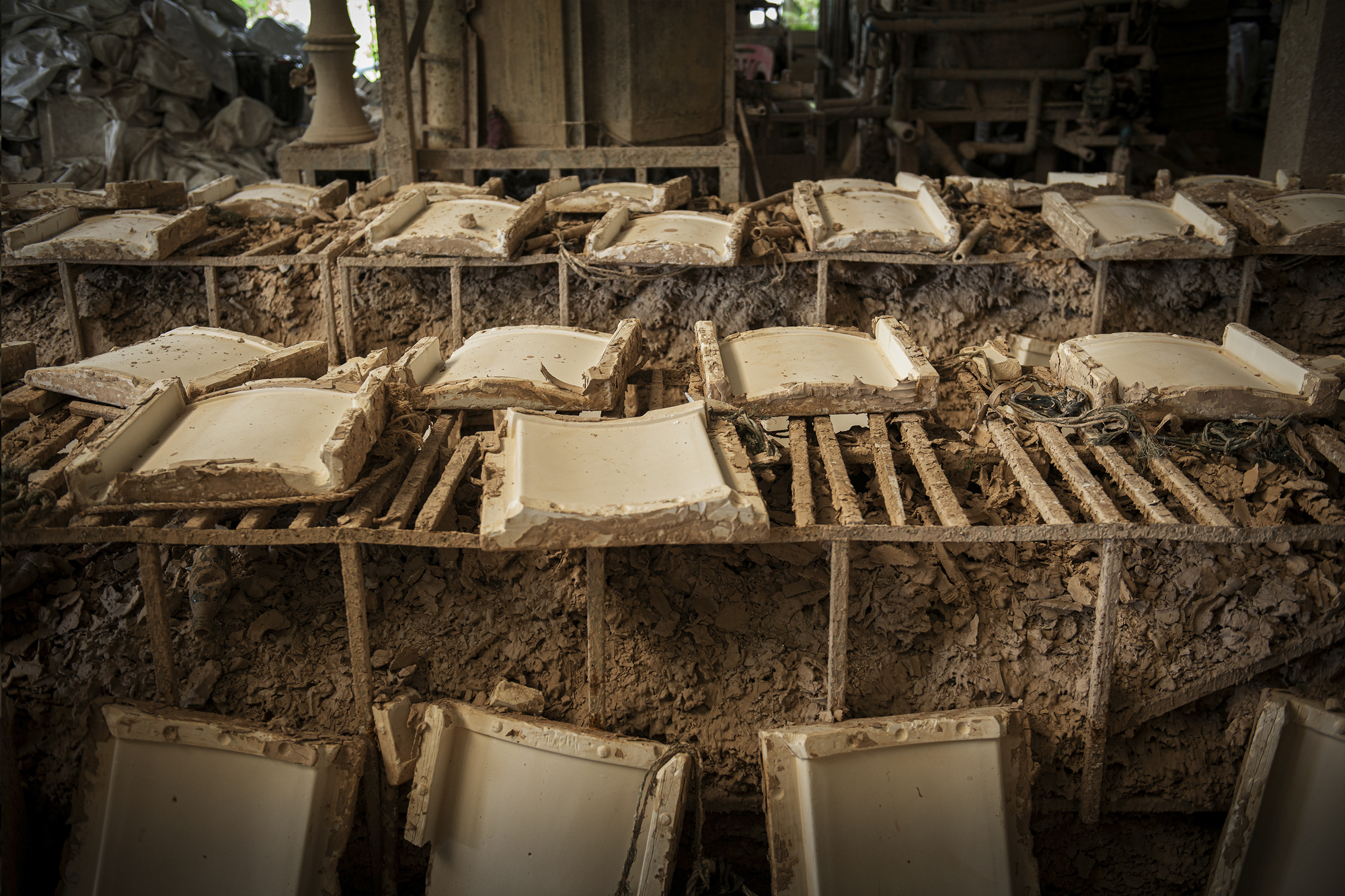 Close-up of stacked ceramic tile molds covered in drying clay and sediment within a workshop interior
