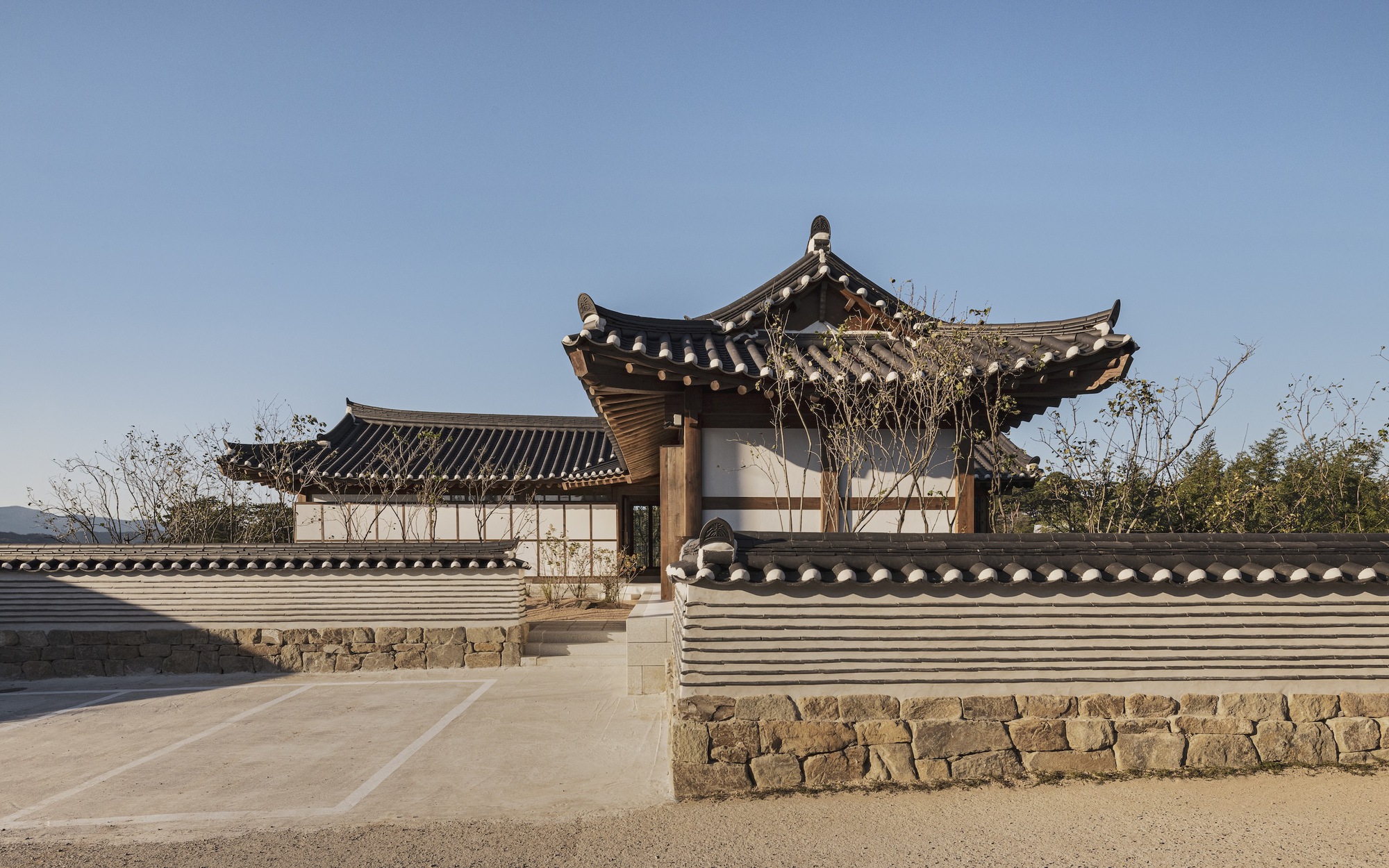 Courtyard entrance with traditional tiled roofs atop stone walls and white plaster under a clear sky