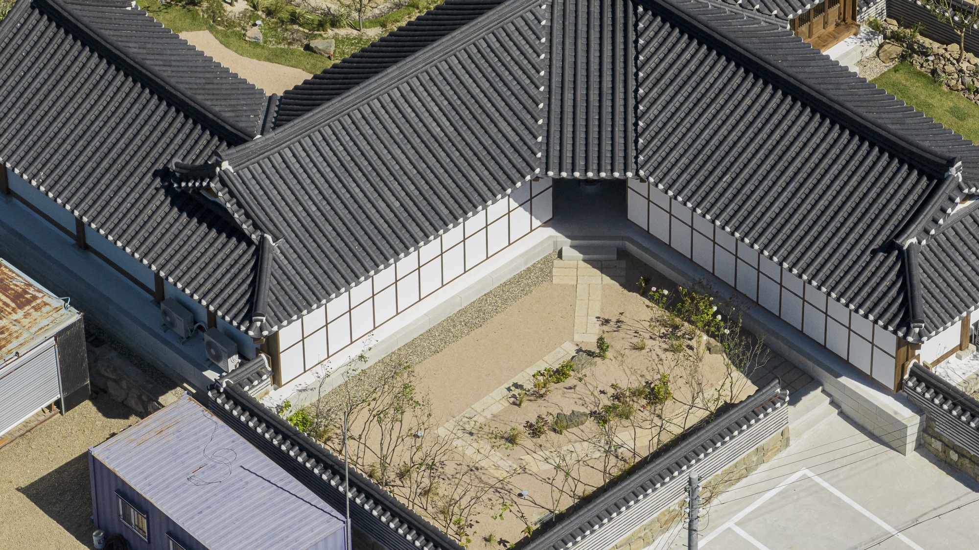 Aerial view of the tiled roofs enclosing a gravel courtyard with young trees and plantings