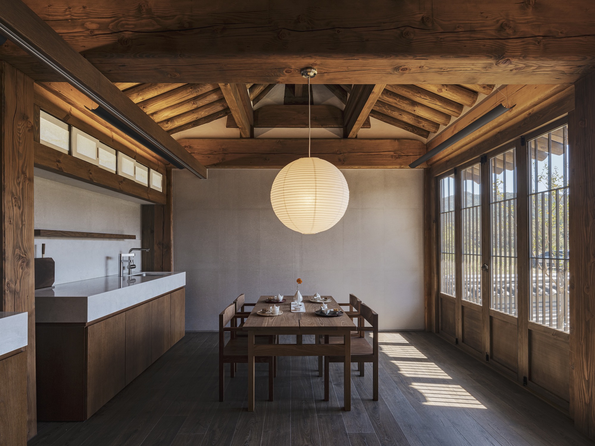 Dining area with exposed timber ceiling beams and paper lantern illuminated by afternoon sunlight