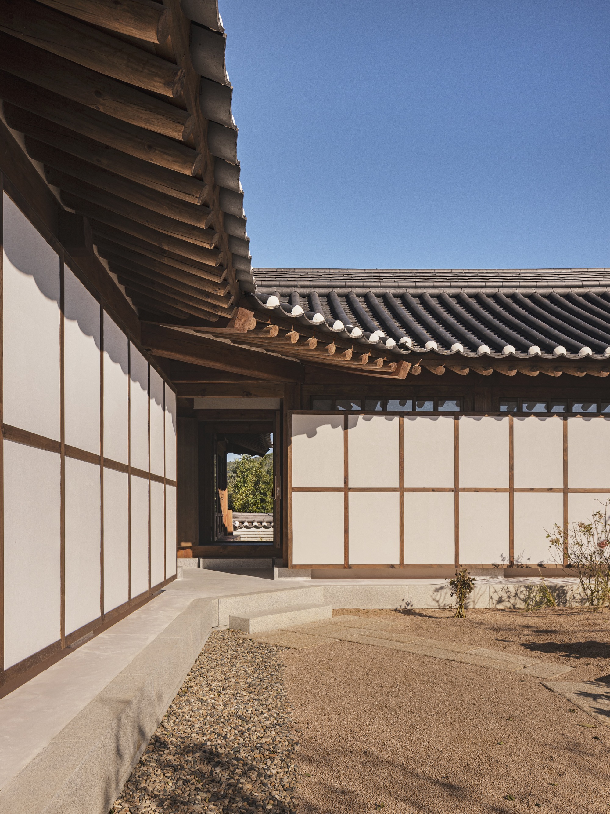 Courtyard passage with translucent screen walls and gravel garden under curved tile roof eaves