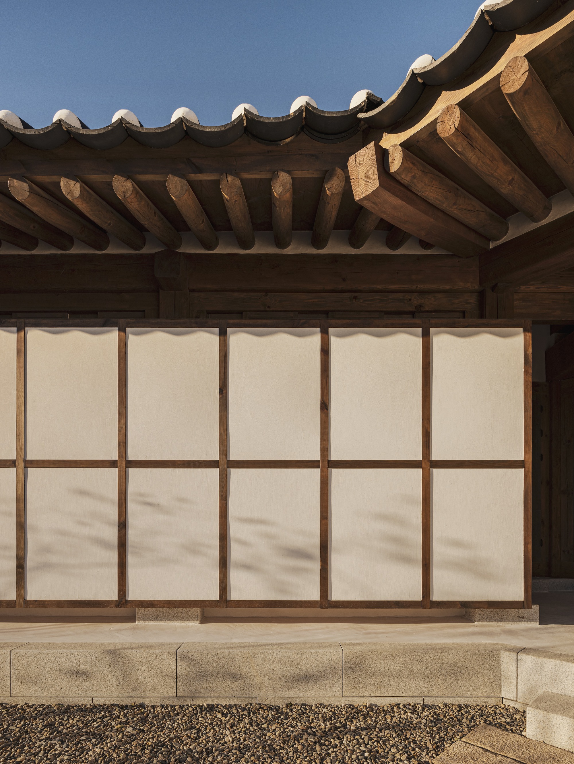 Exterior wall with translucent paper panels in timber frames below a tiled eave with exposed rafters