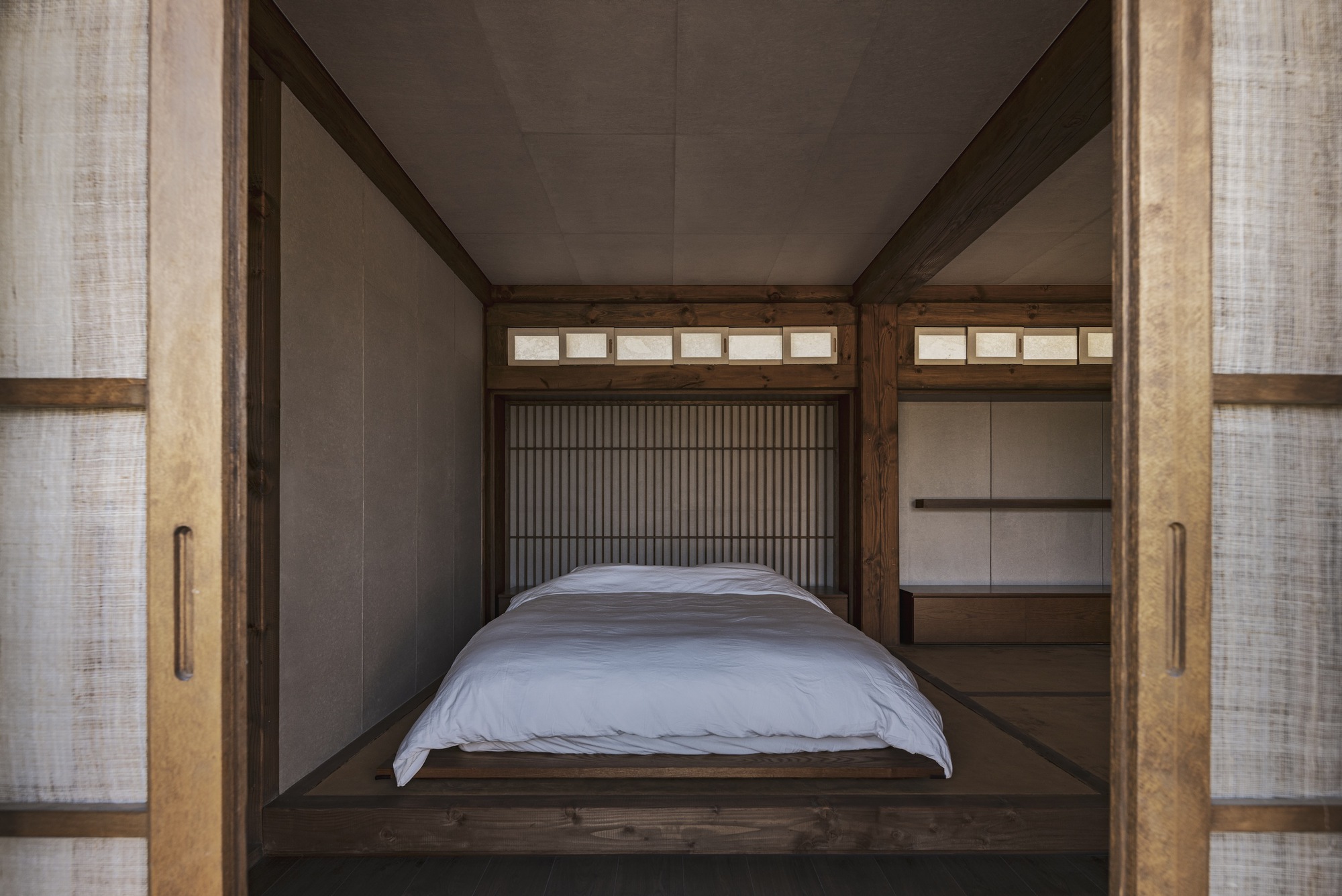 Platform bed framed by timber posts with vertical slat screens and translucent sliding panels