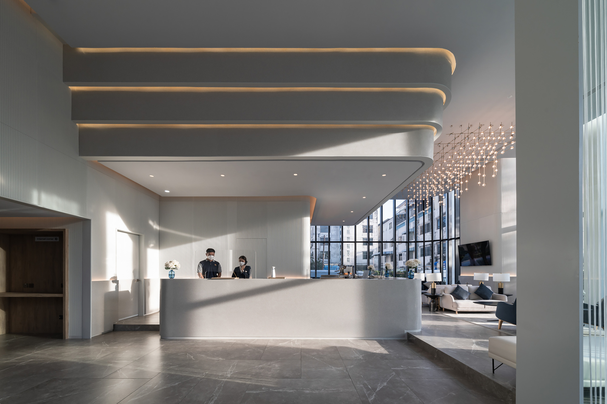 Double-height lobby with curved reception desk and layered ceiling coves with recessed lighting