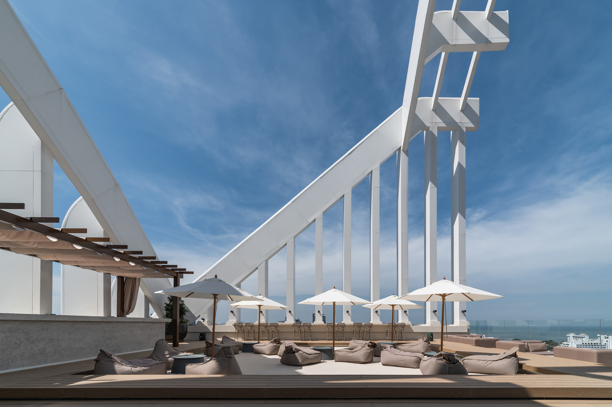Rooftop lounge deck with white umbrellas and cushioned seating beneath angled white structural blades