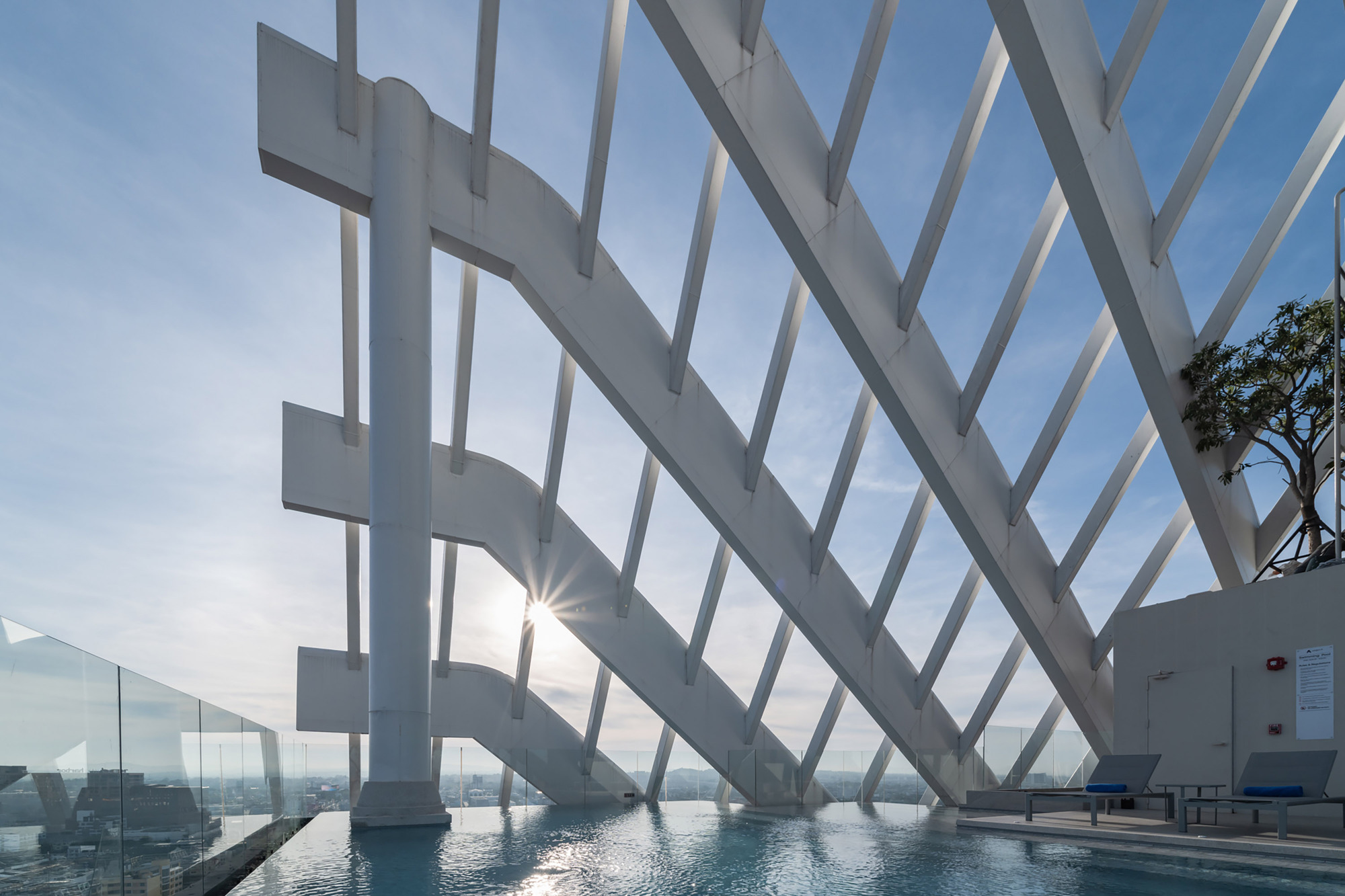 White diagonal structural ribs forming a sheltered terrace with a reflecting pool at sunrise