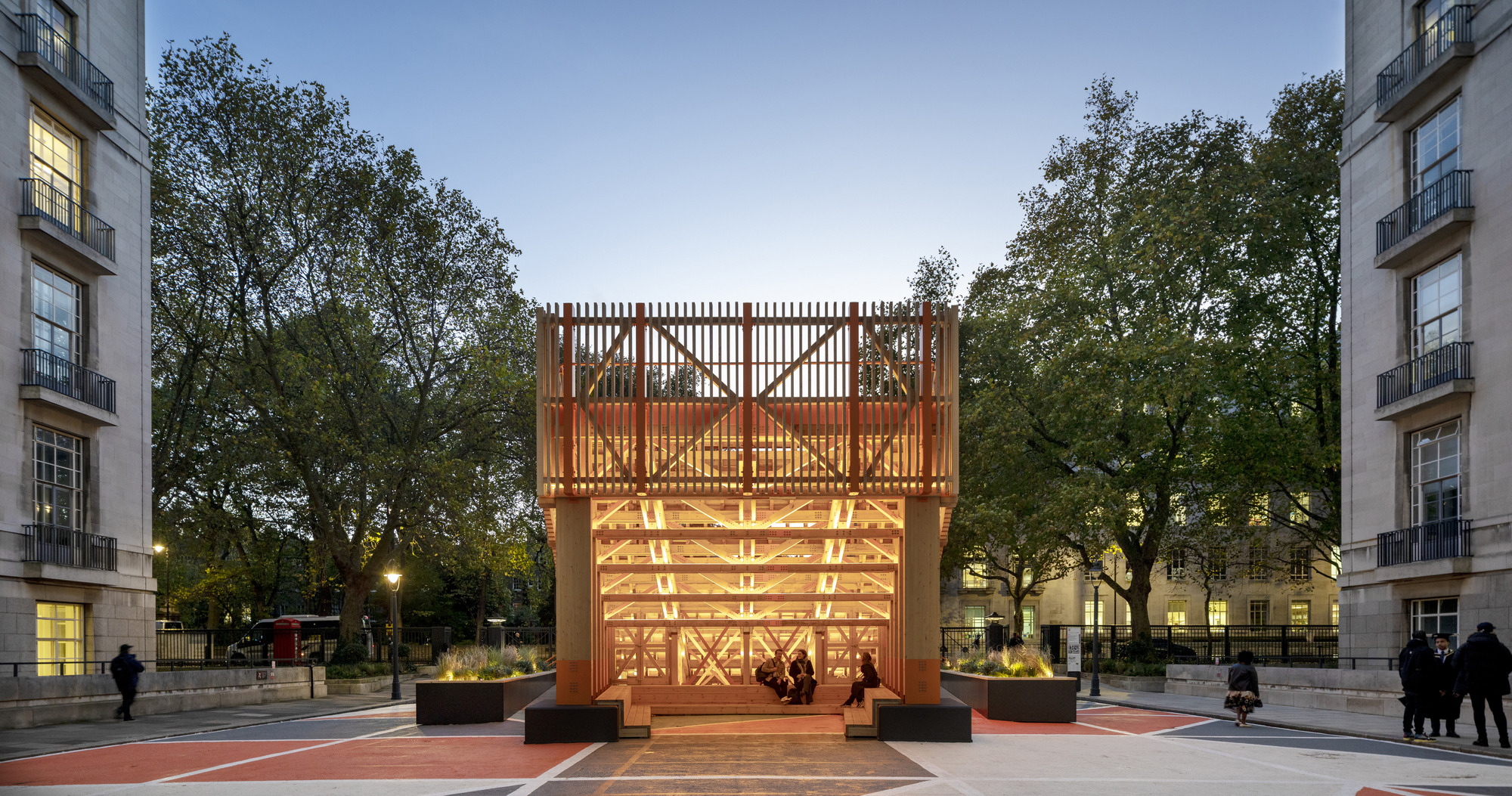 Front elevation of the illuminated timber structure set between trees at twilight