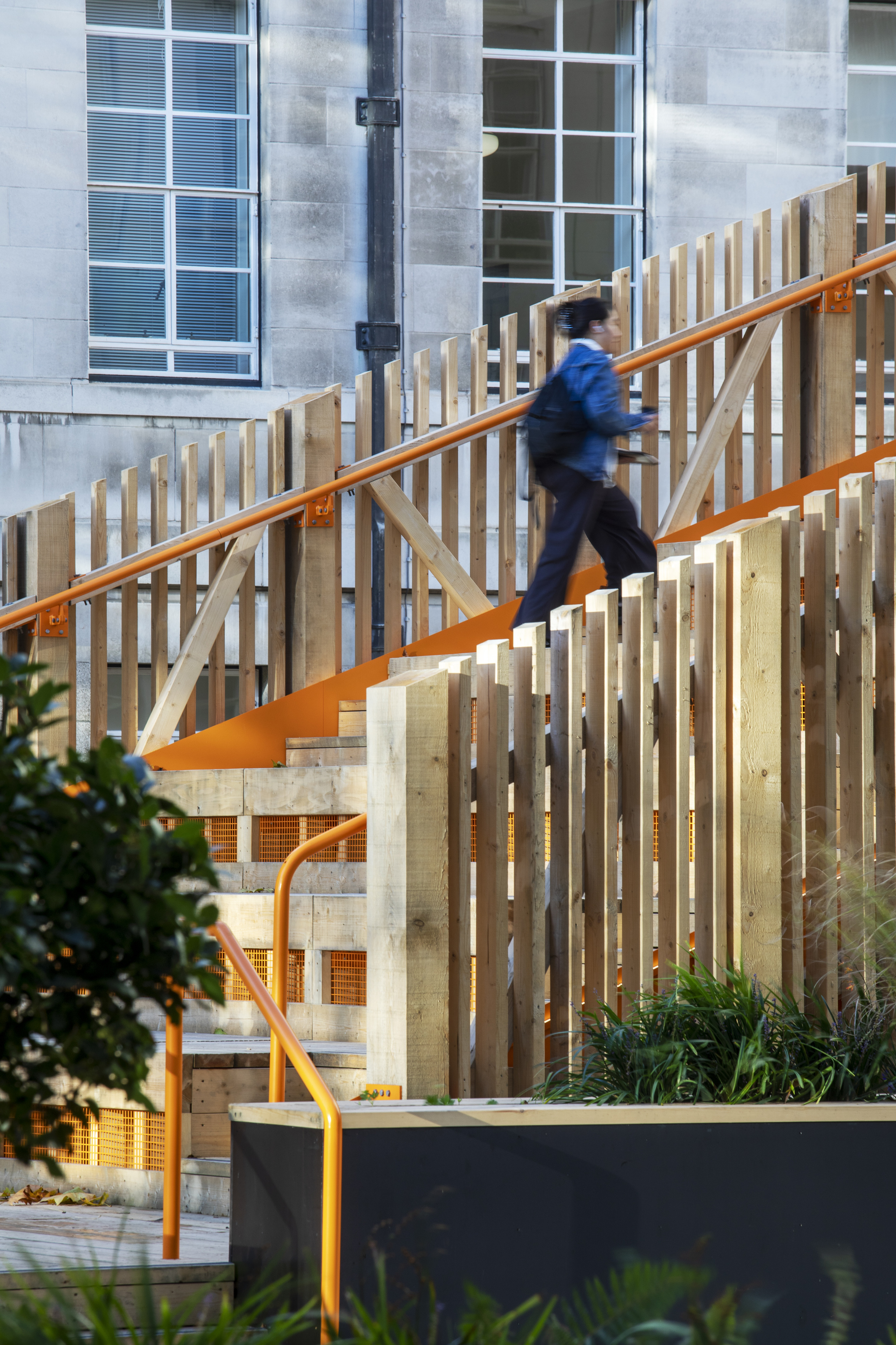 Person in motion ascending the staircase with vertical slatted timber balustrade and planted beds below