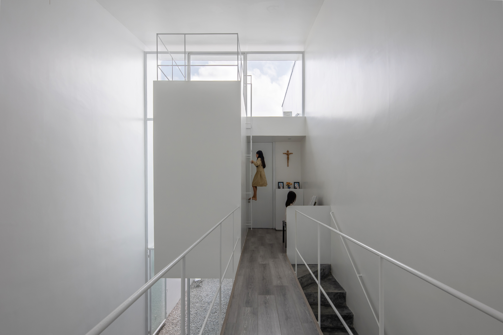 Double-height interior space with a bridge and figure on upper level illuminated by skylight