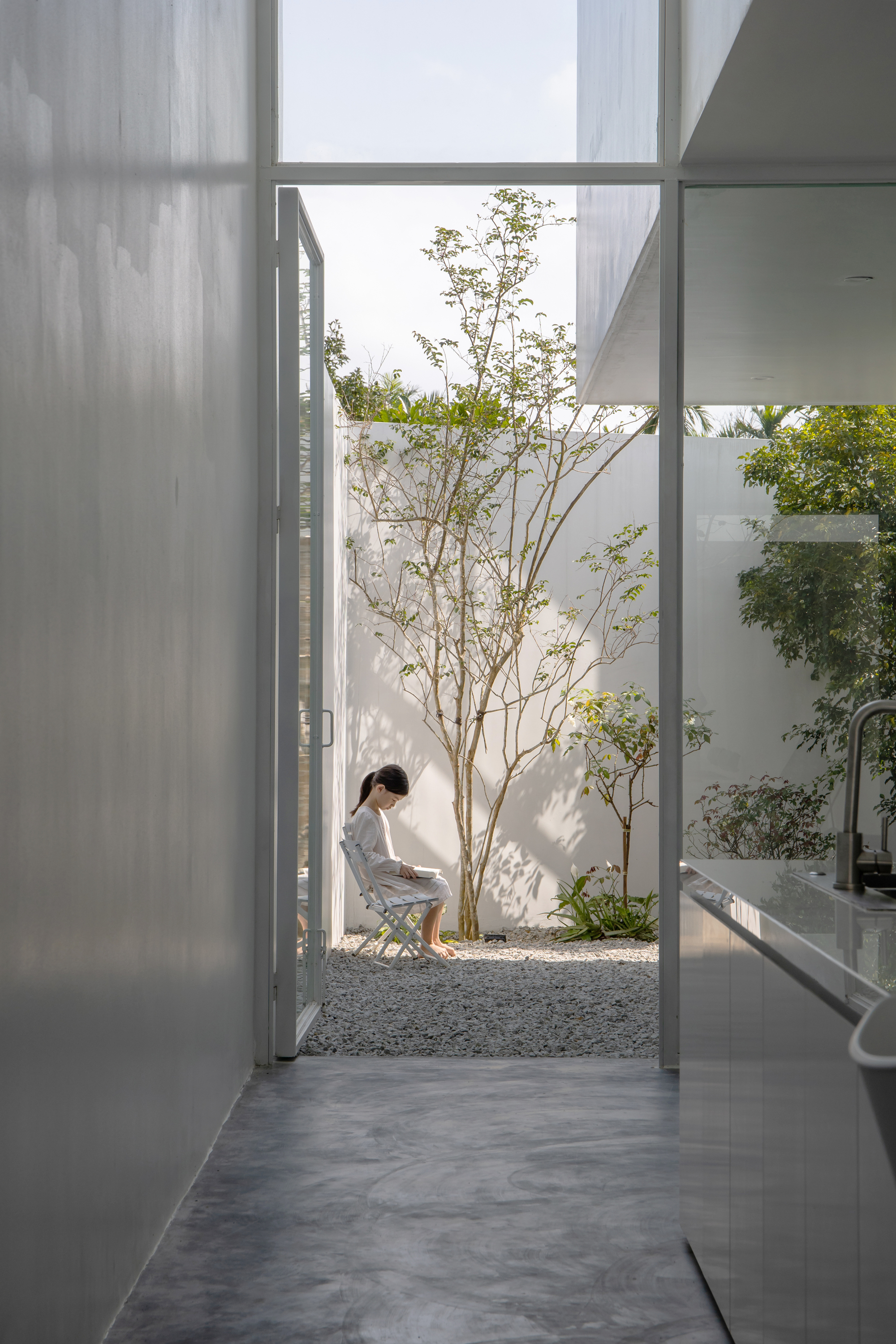 View from a bathroom through sheer curtains to a gravel courtyard where a person sits