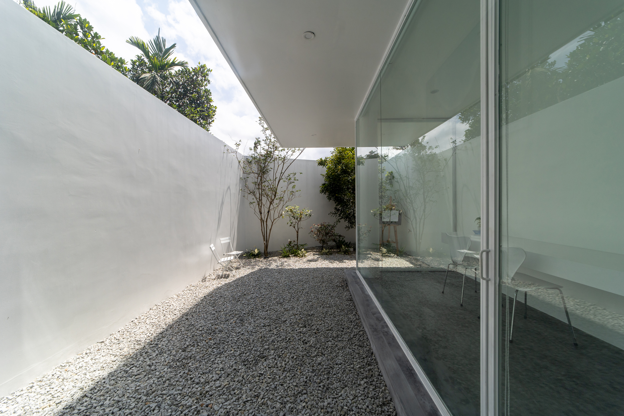 Enclosed courtyard with gravel floor and floor-to-ceiling glass wall under partial shade