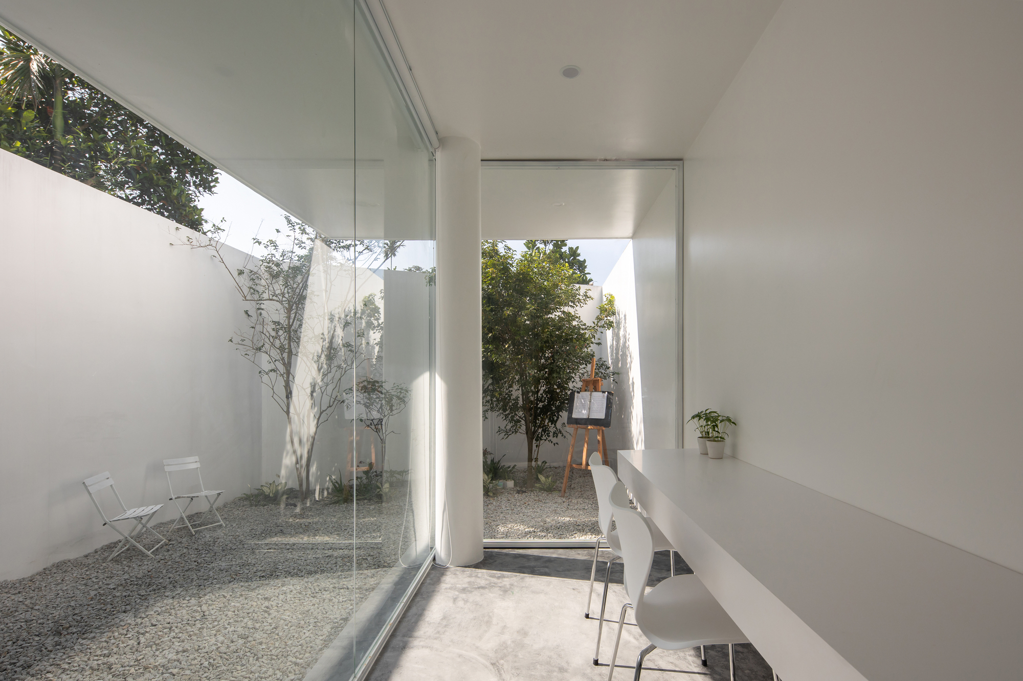 Interior view through glass walls toward twin gravel courtyards with planted trees