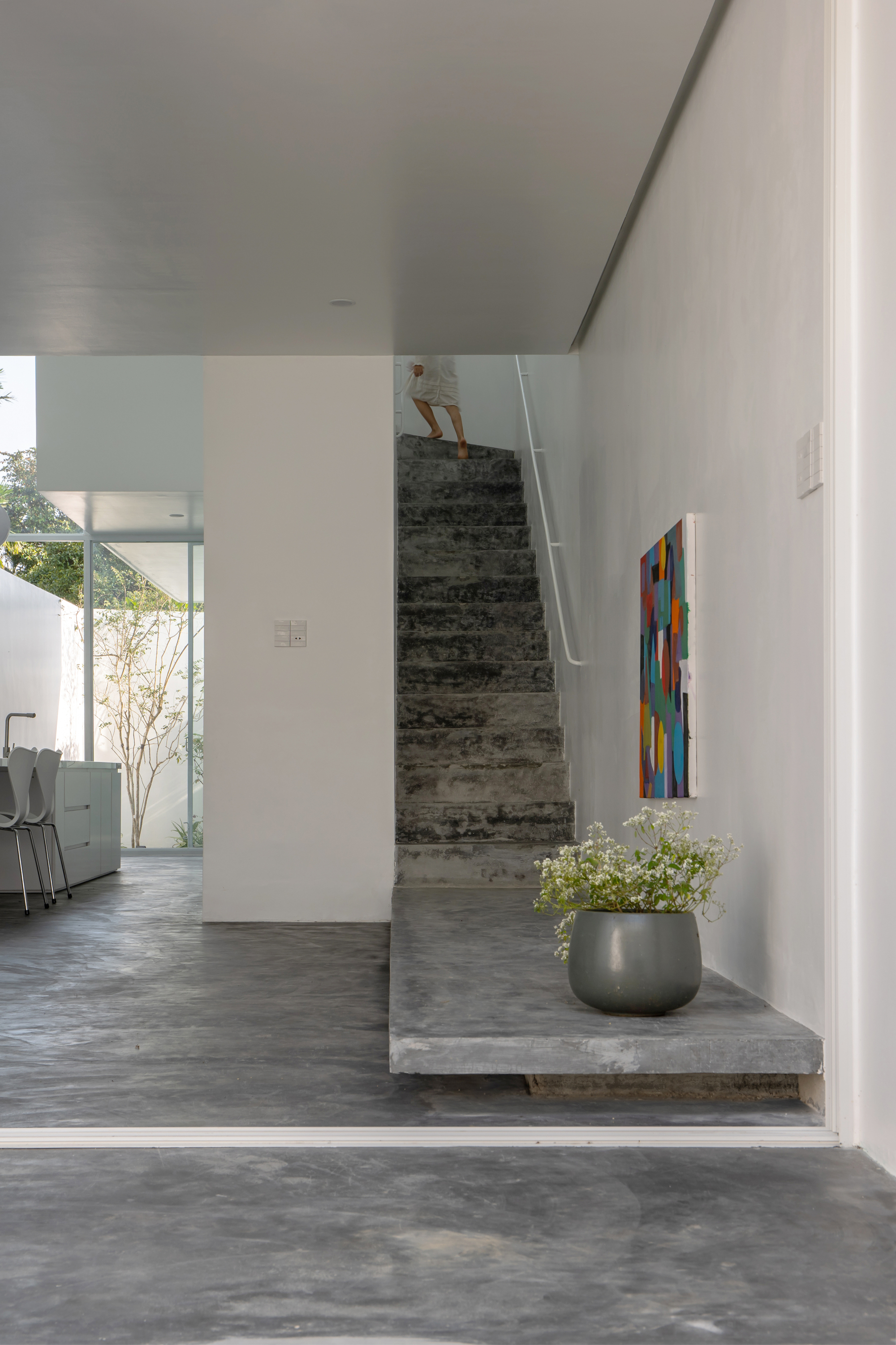Board-formed concrete staircase rising from the living area with a figure ascending