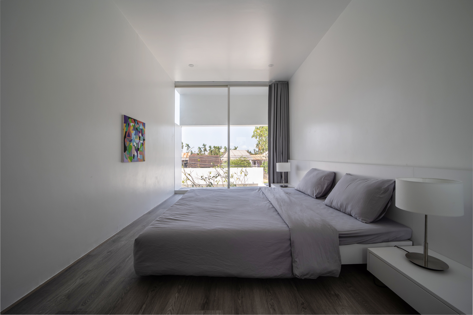 Bedroom with grey timber flooring and full-height window overlooking courtyard greenery