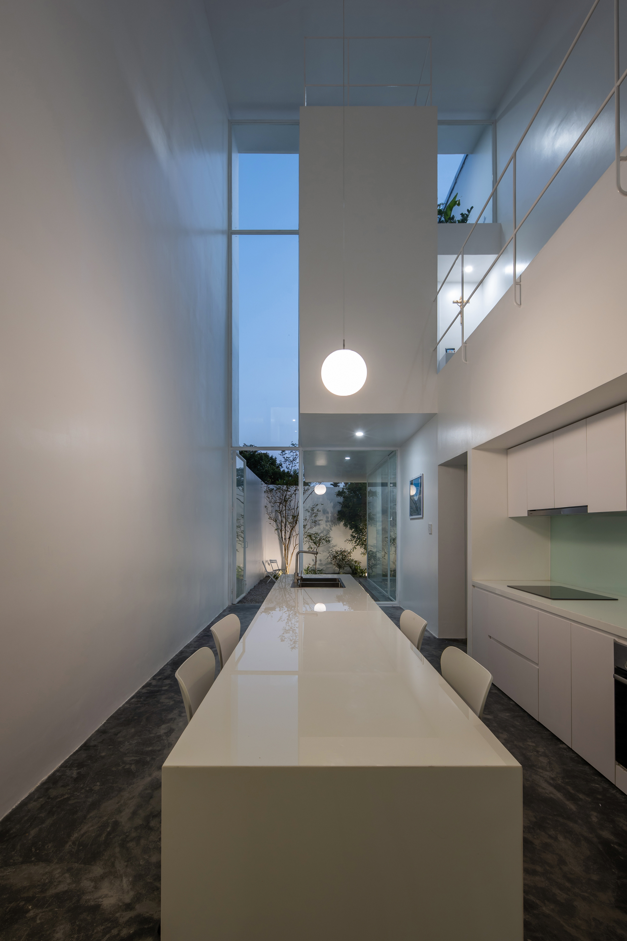 Double-height dining space with a suspended globe pendant and view to the planted courtyard beyond