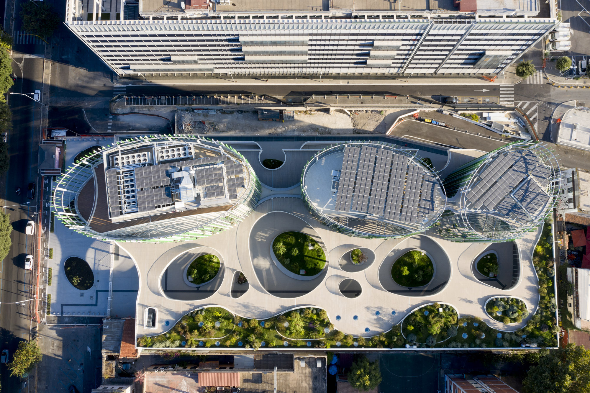 Aerial view of the curved roof plane with circular skylights and planted openings adjacent to striped canopy structure