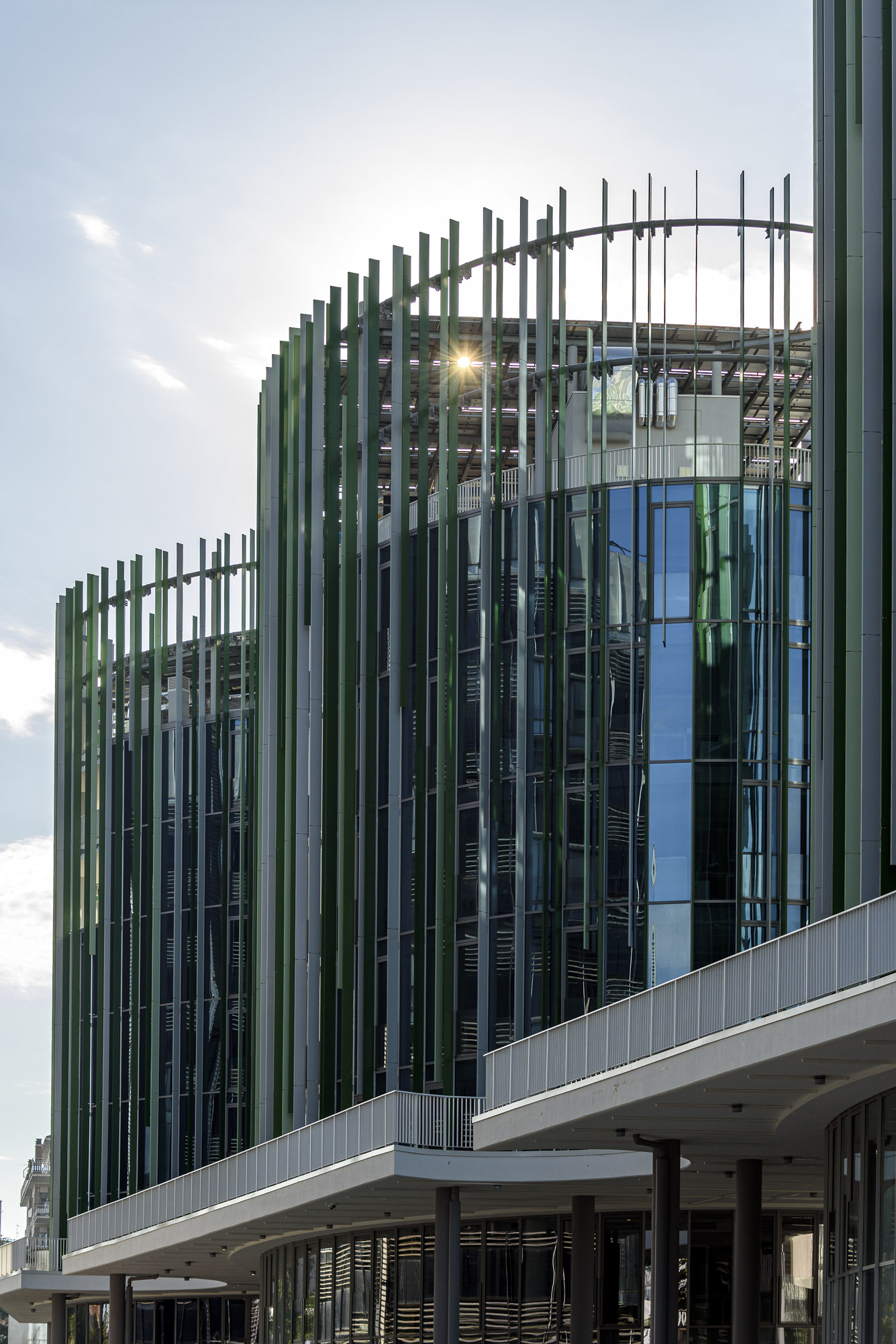 Facade detail of vertical green and blue louvres wrapping curved glass volumes at dusk