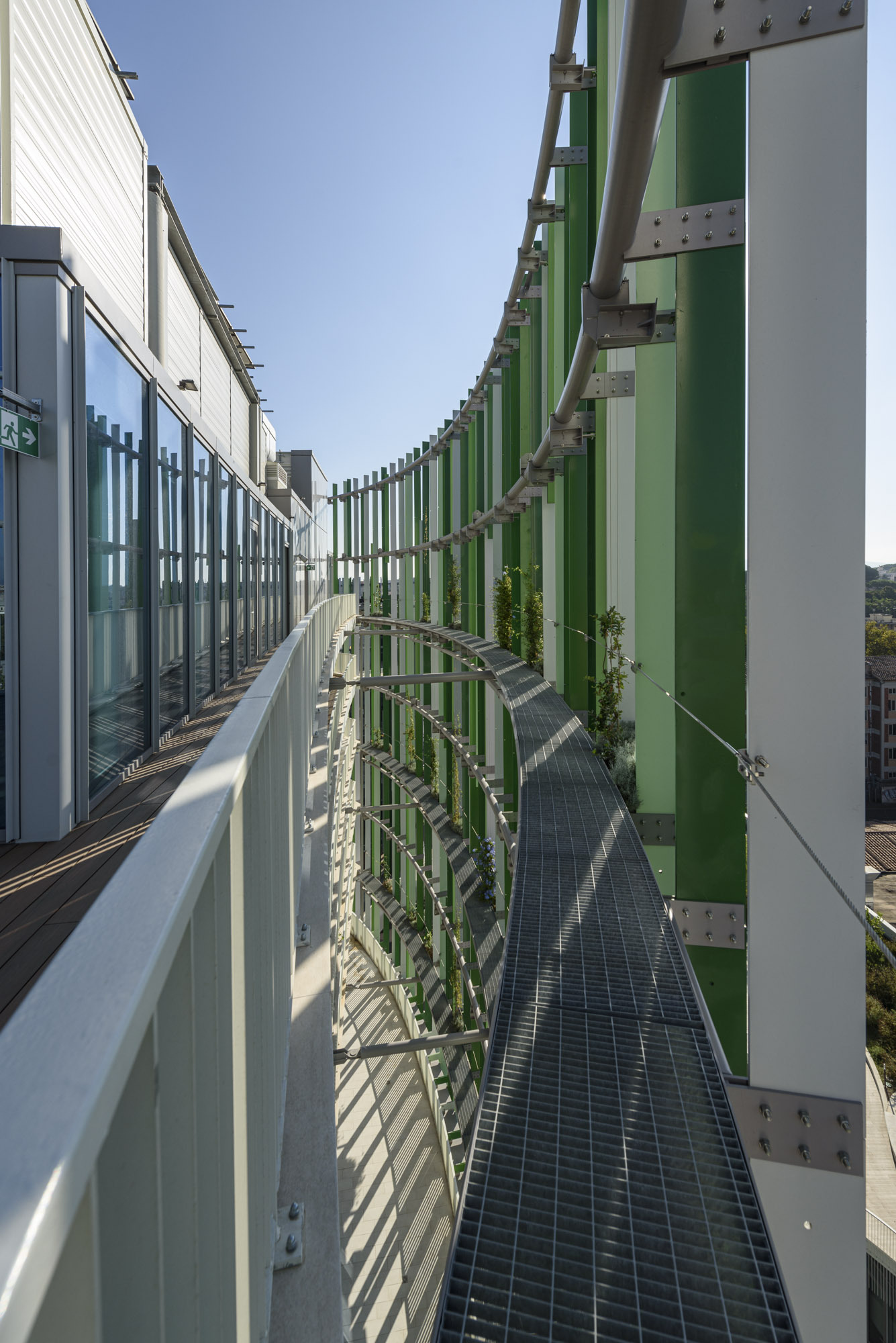 Exterior maintenance walkway with green vertical fins and climbing plants along the curved perimeter