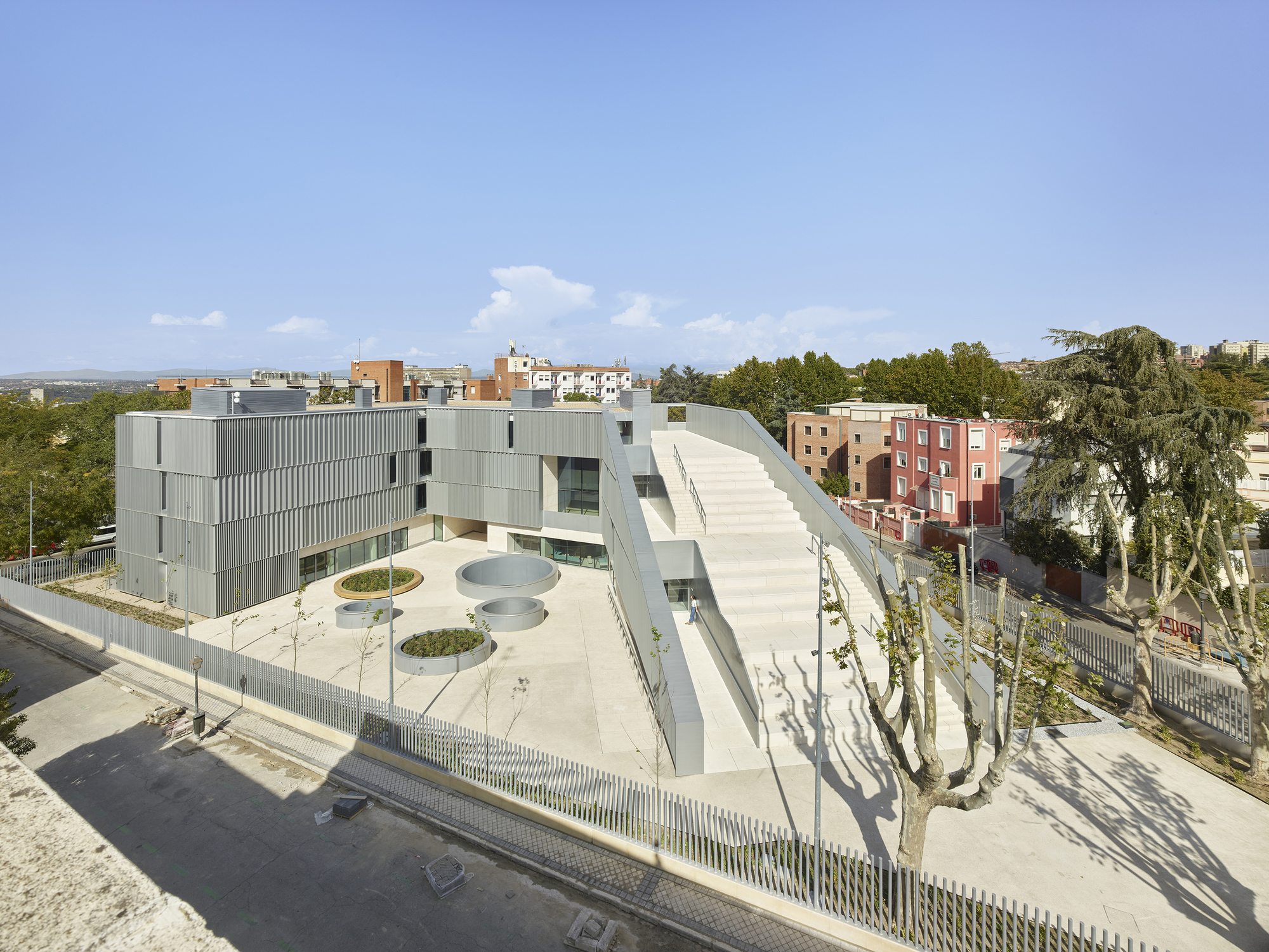 Elevated view of the triangular courtyard with circular planters and the metal-clad volumes surrounded by trees