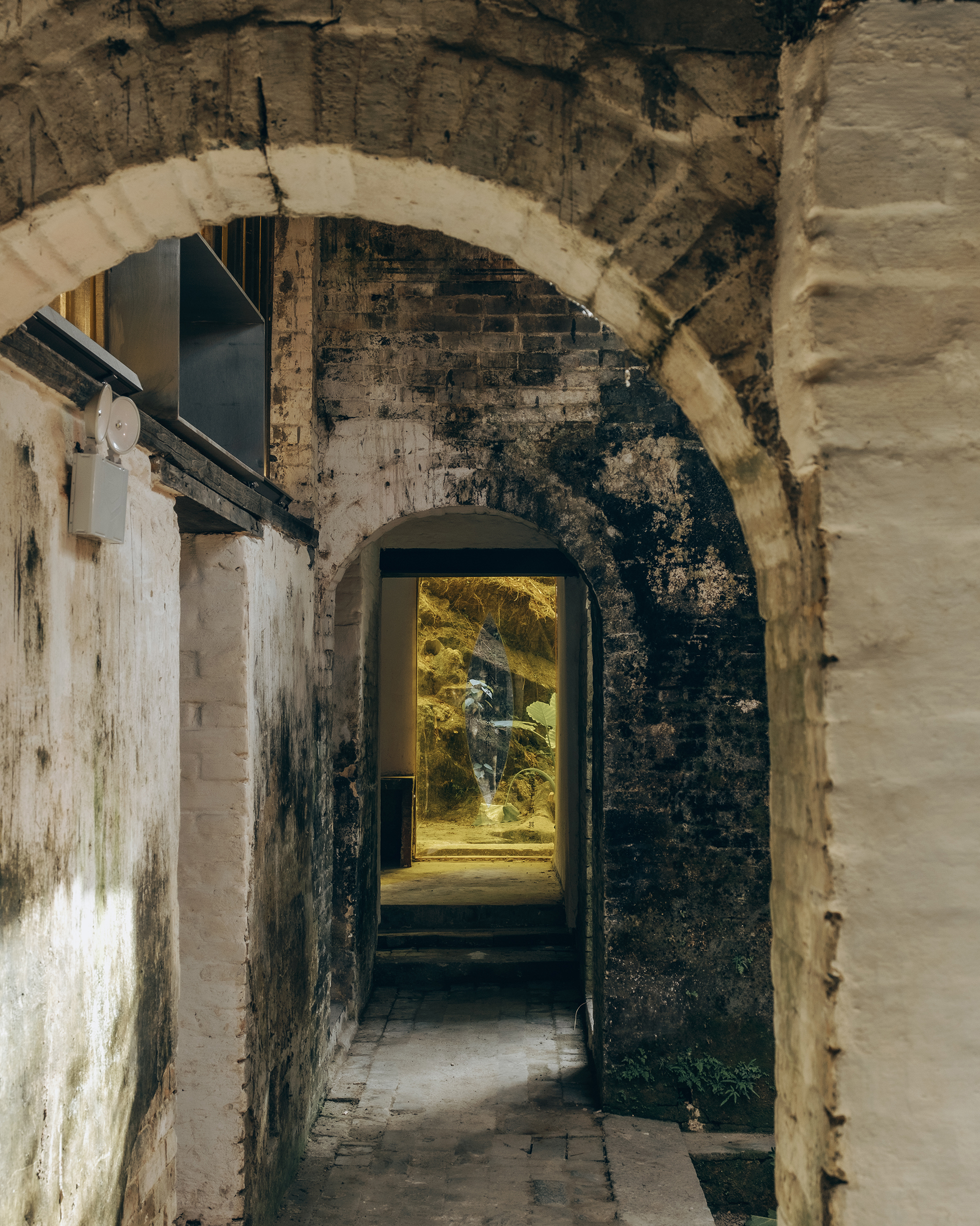 Sequence of brick arches framing a passageway with warm sunlight illuminating the far courtyard