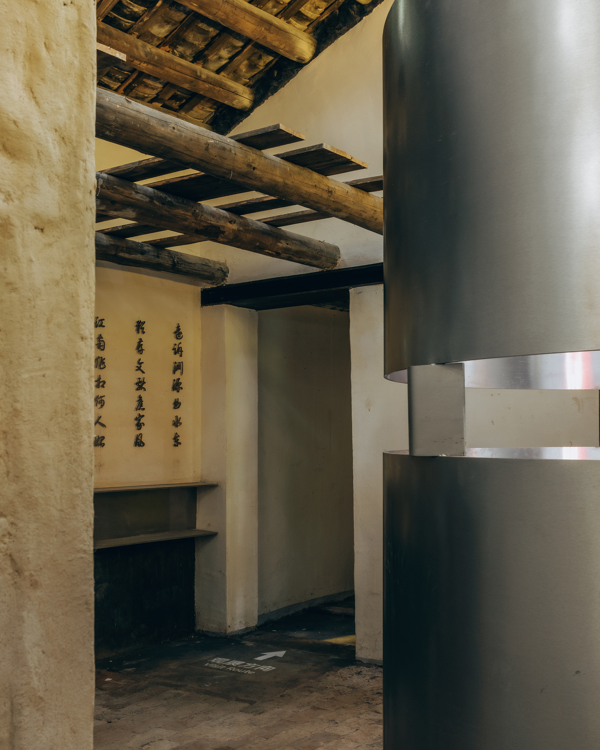 Interior room with exposed timber ceiling beams and a cylindrical metal ventilation duct beside calligraphy panels
