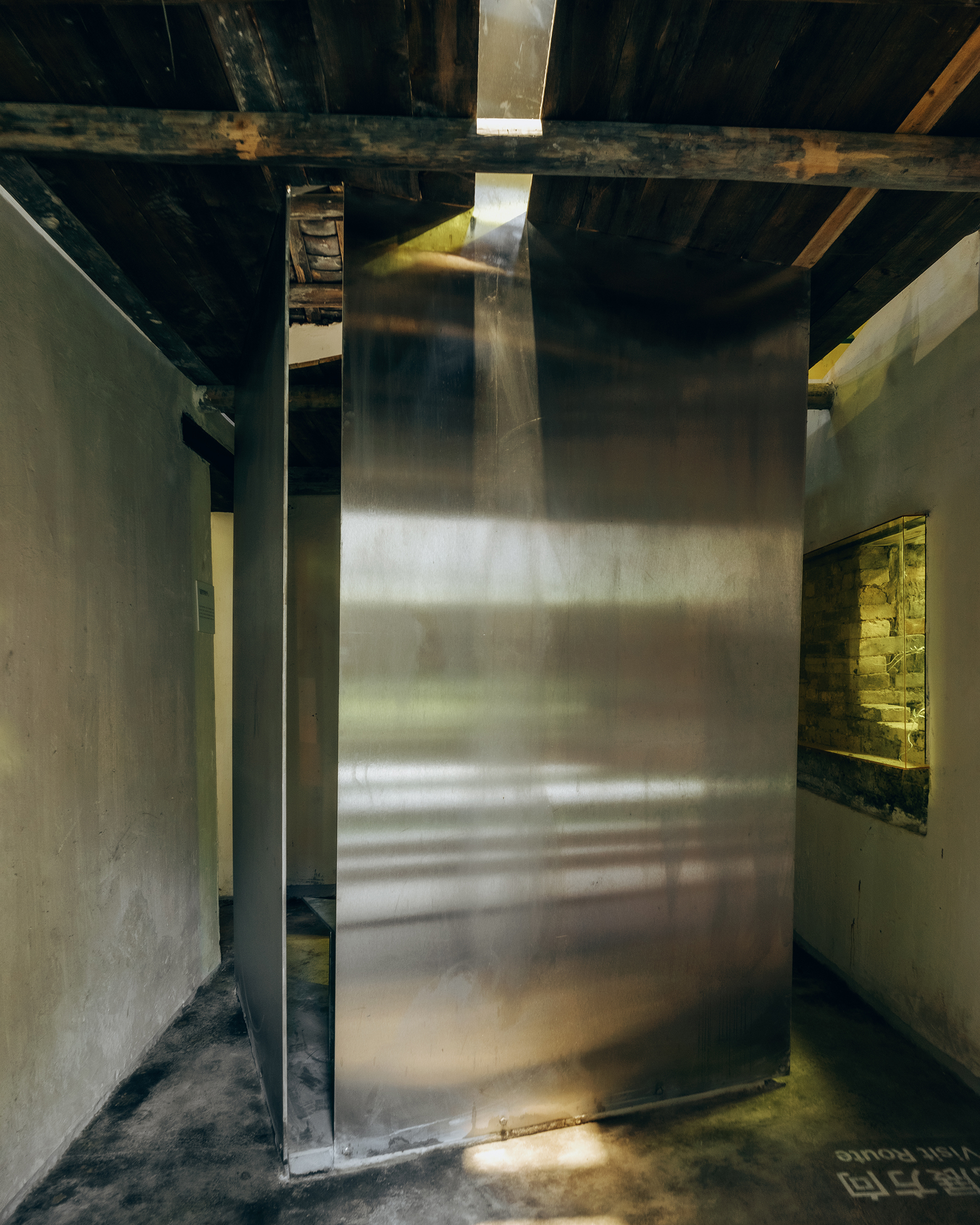 Brass wall panel rising through exposed timber ceiling joists with light from above