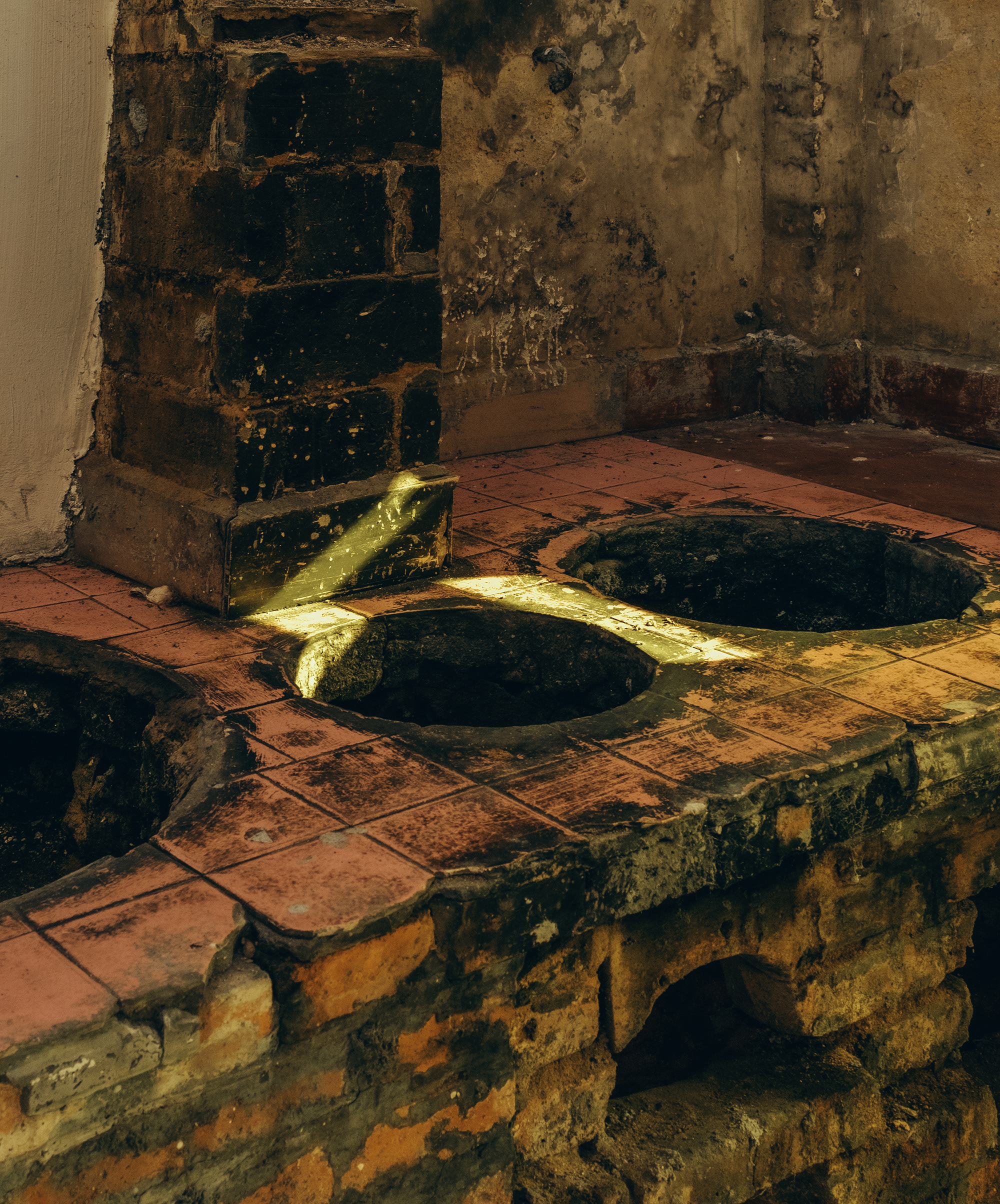 Terracotta tile stove with circular brass burner openings beside a deteriorated wall