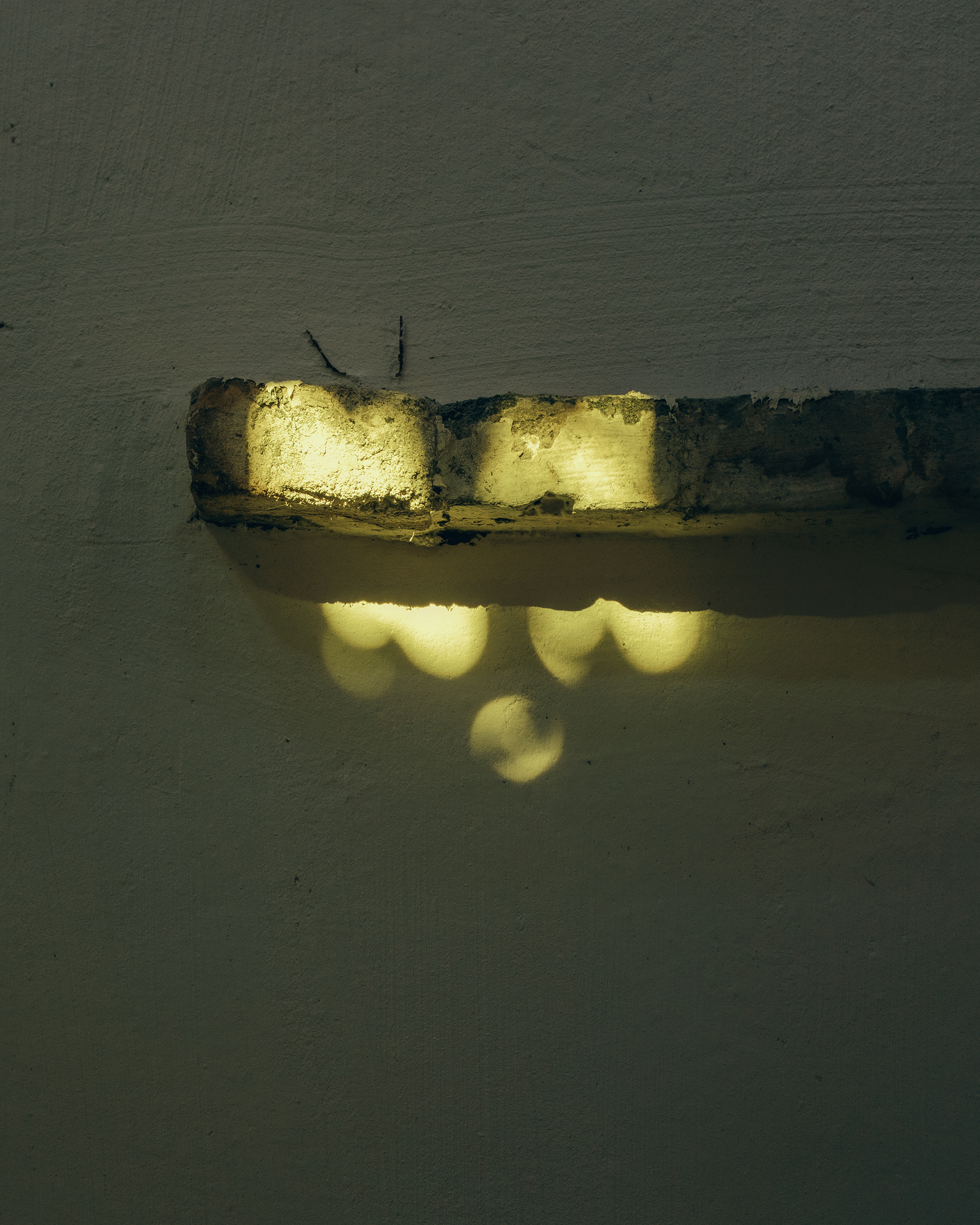 Illuminated brick ledge casting yellow light and shadow patterns on plaster wall