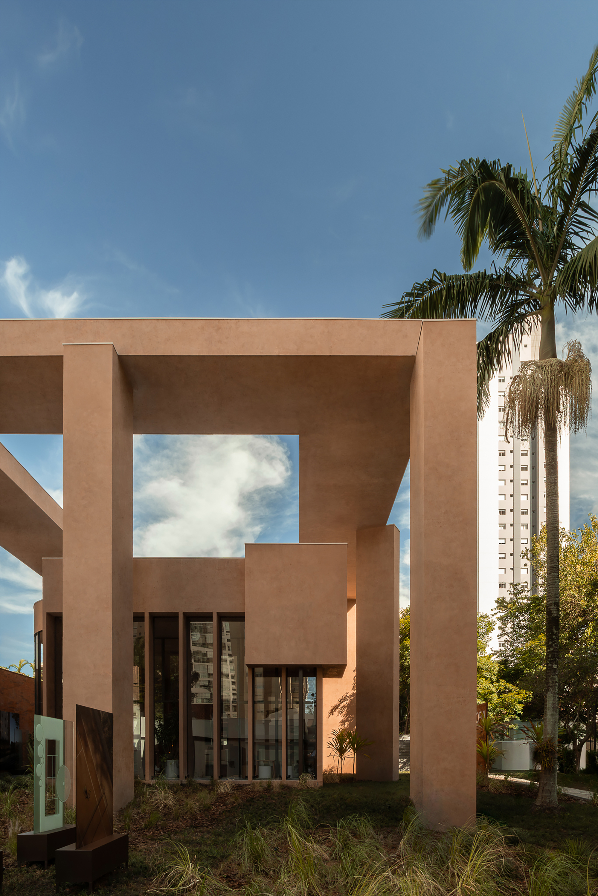 Portal-like terracotta frame structure surrounding glazed entrance with palm trees beyond