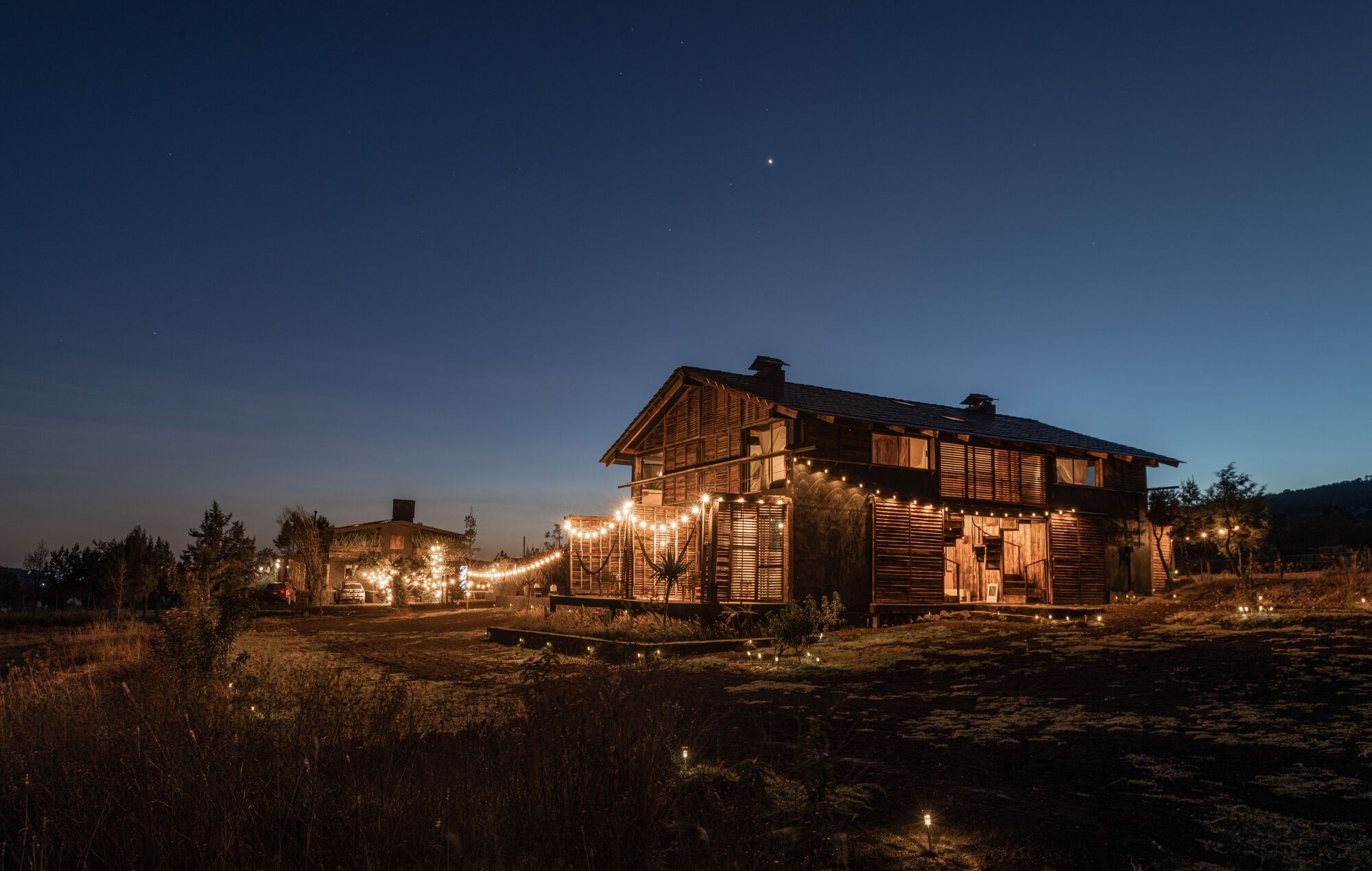 Weathered timber facade with strung lights across the exterior at twilight under a darkening sky