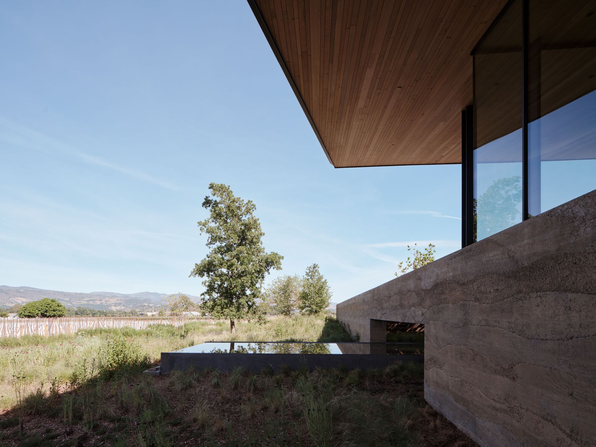Cantilever timber soffit above board-formed concrete retaining wall overlooking vineyard and distant hills