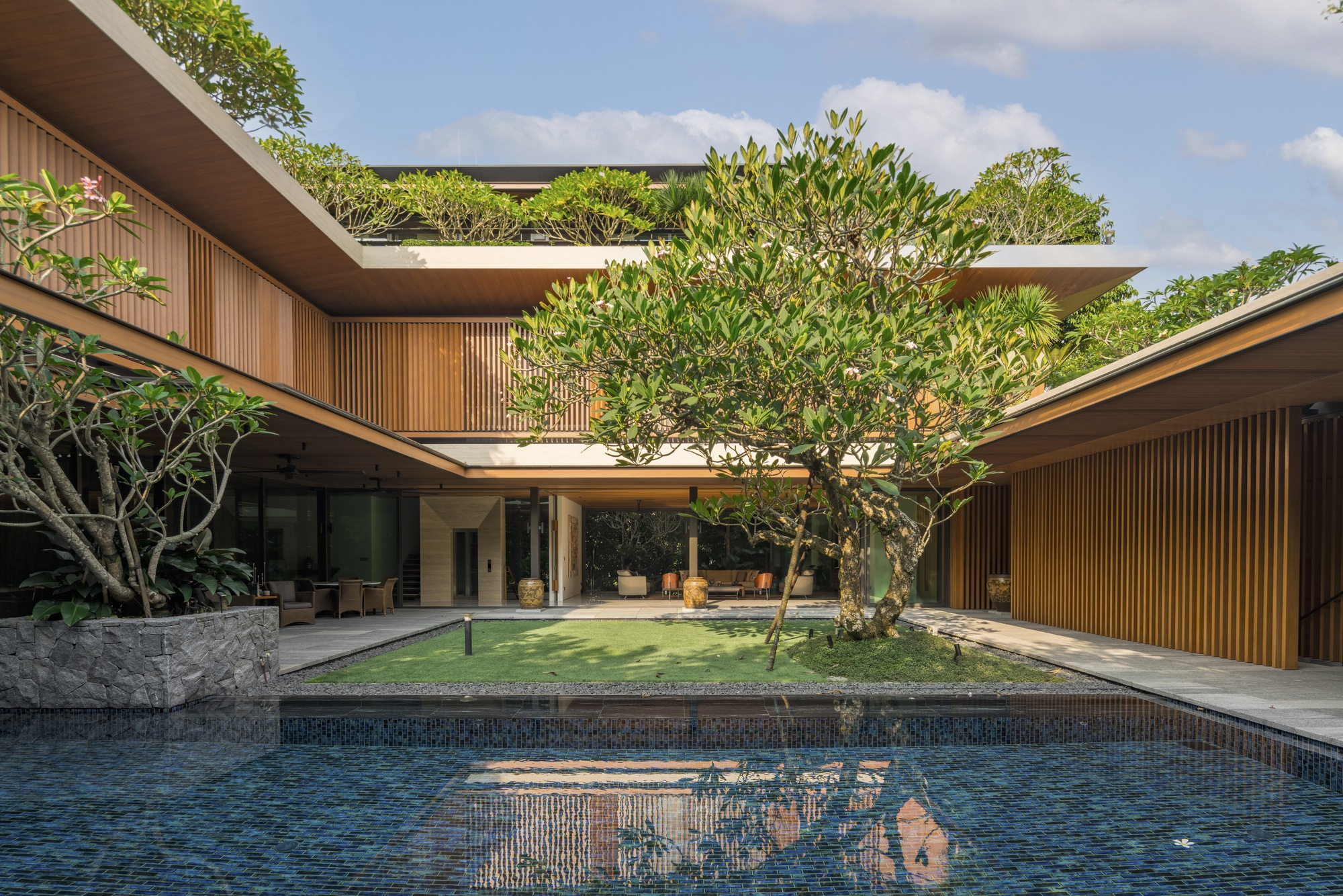 Courtyard view with central pool, vertical timber cladding, and rooftop gardens framing a central tree