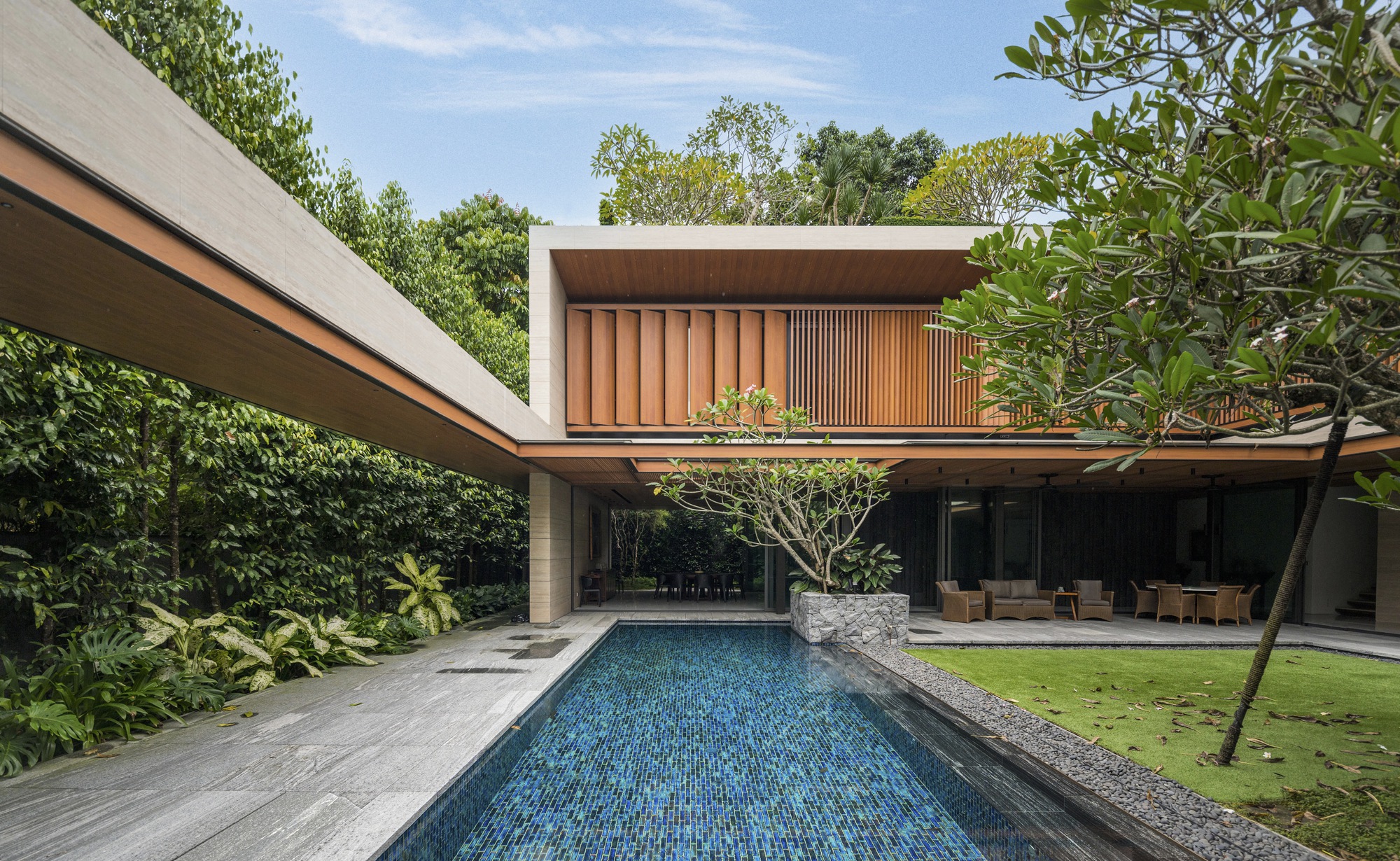 Blue mosaic-tiled pool extending toward timber-clad volumes with glass walls and planted roofs