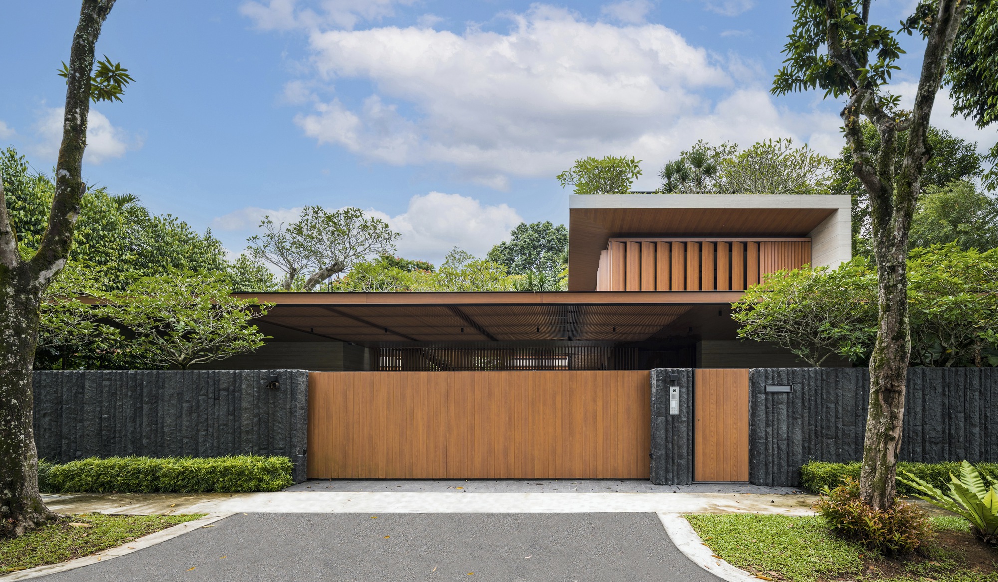 Street facade with timber cladding and dark stone boundary wall beneath a partly cloudy sky