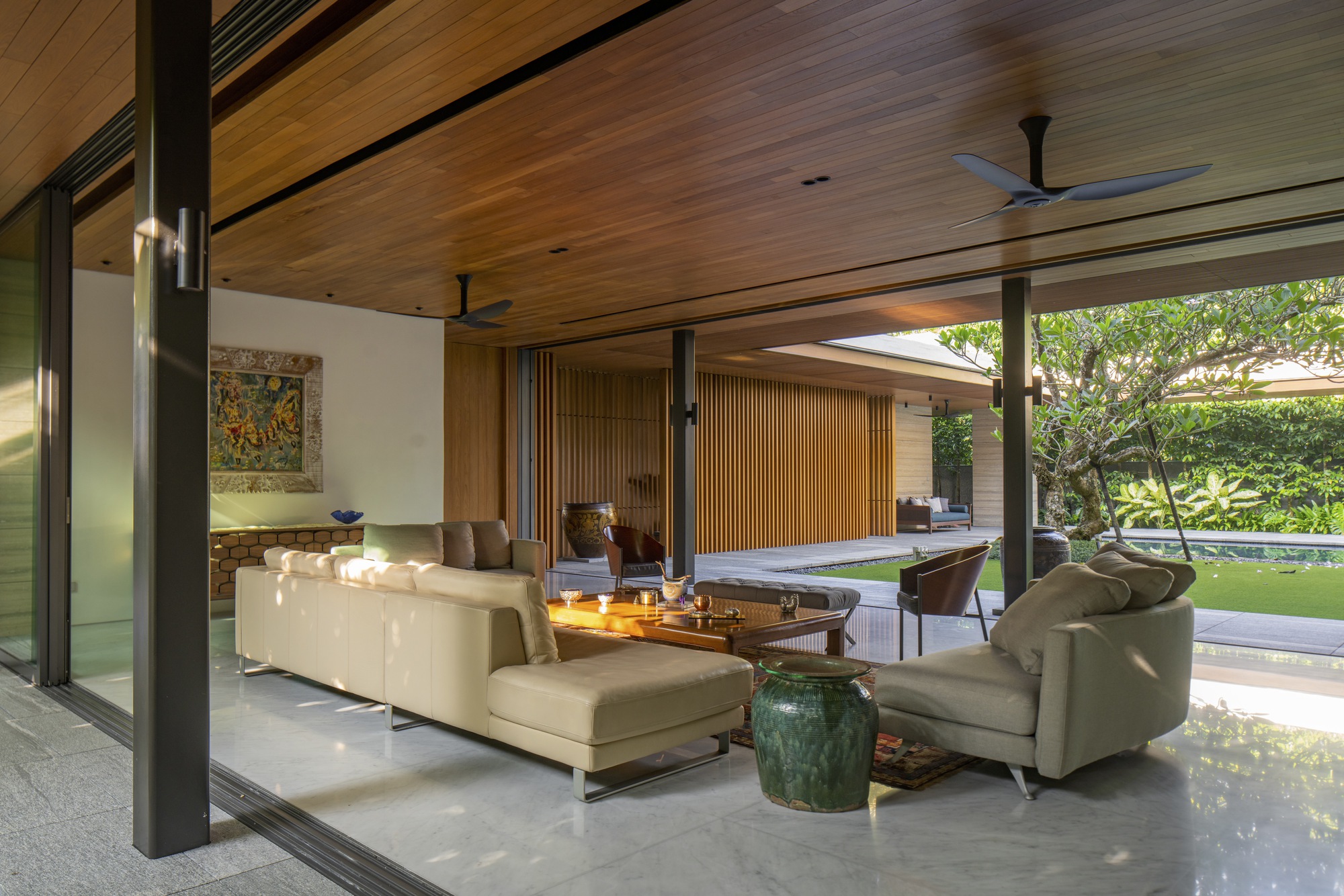 Living room with black steel columns and timber ceiling opening to the garden through full-height glazing