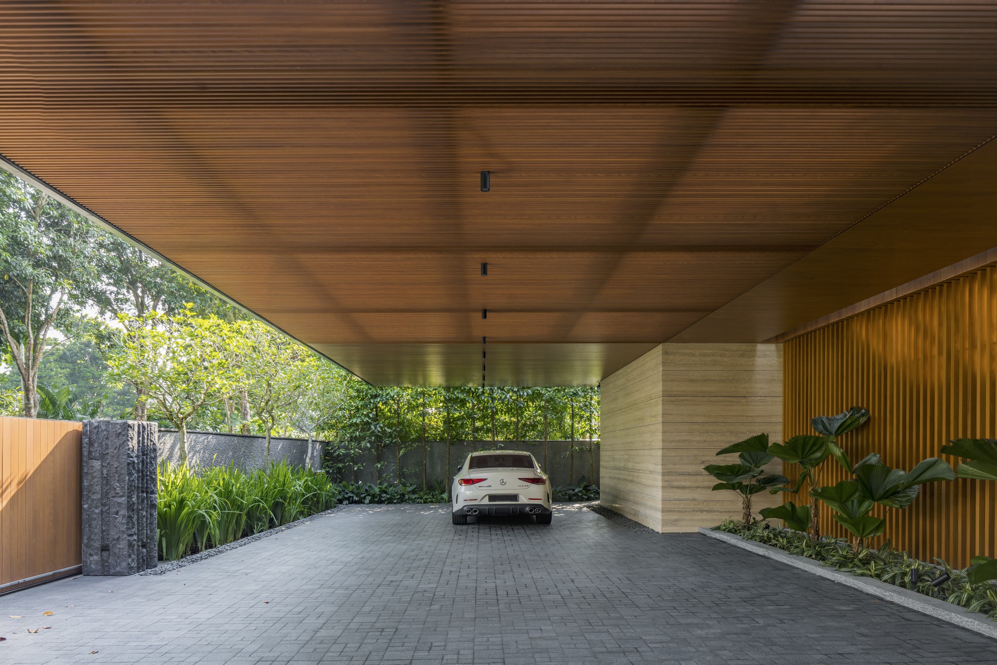 Covered carport with slatted timber ceiling and stone-clad columns framing a vehicle entrance
