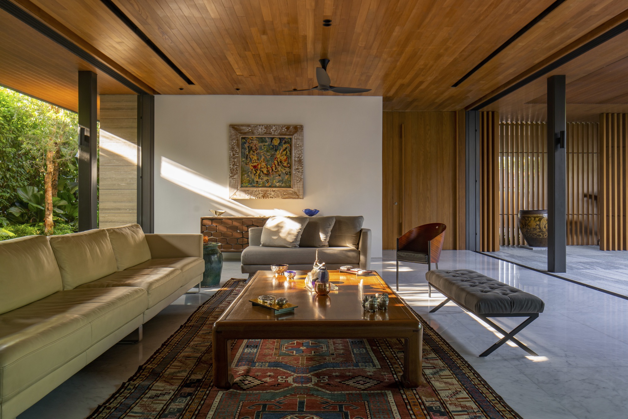 Living room with timber ceiling and full-height glazing opening to a garden courtyard in afternoon light