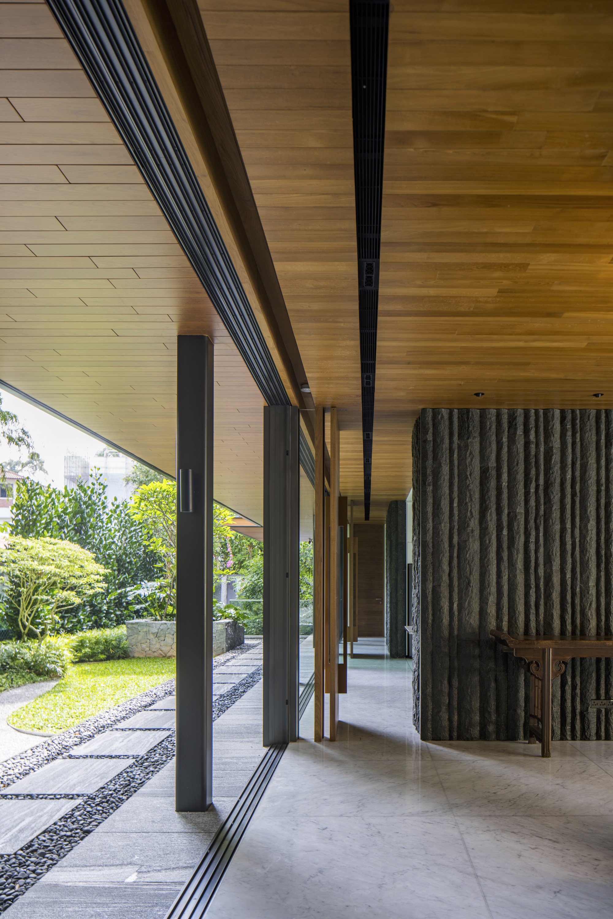 Covered walkway with timber-clad soffit and concrete flooring alongside a gravel garden path