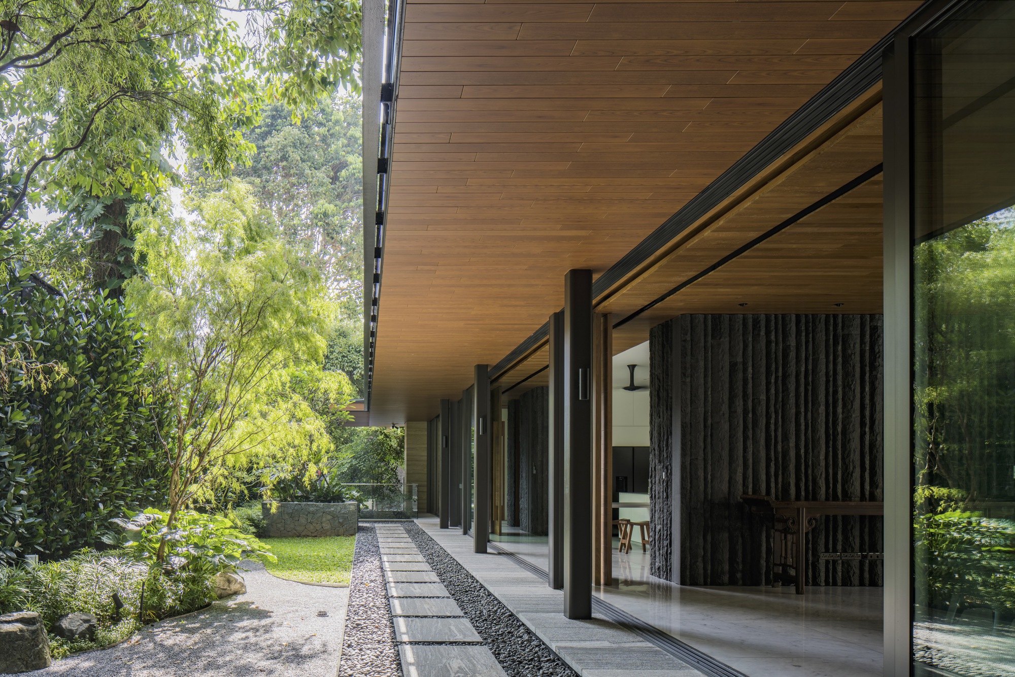 Deep overhang with timber ceiling sheltering a glazed corridor and garden with bamboo and lawn