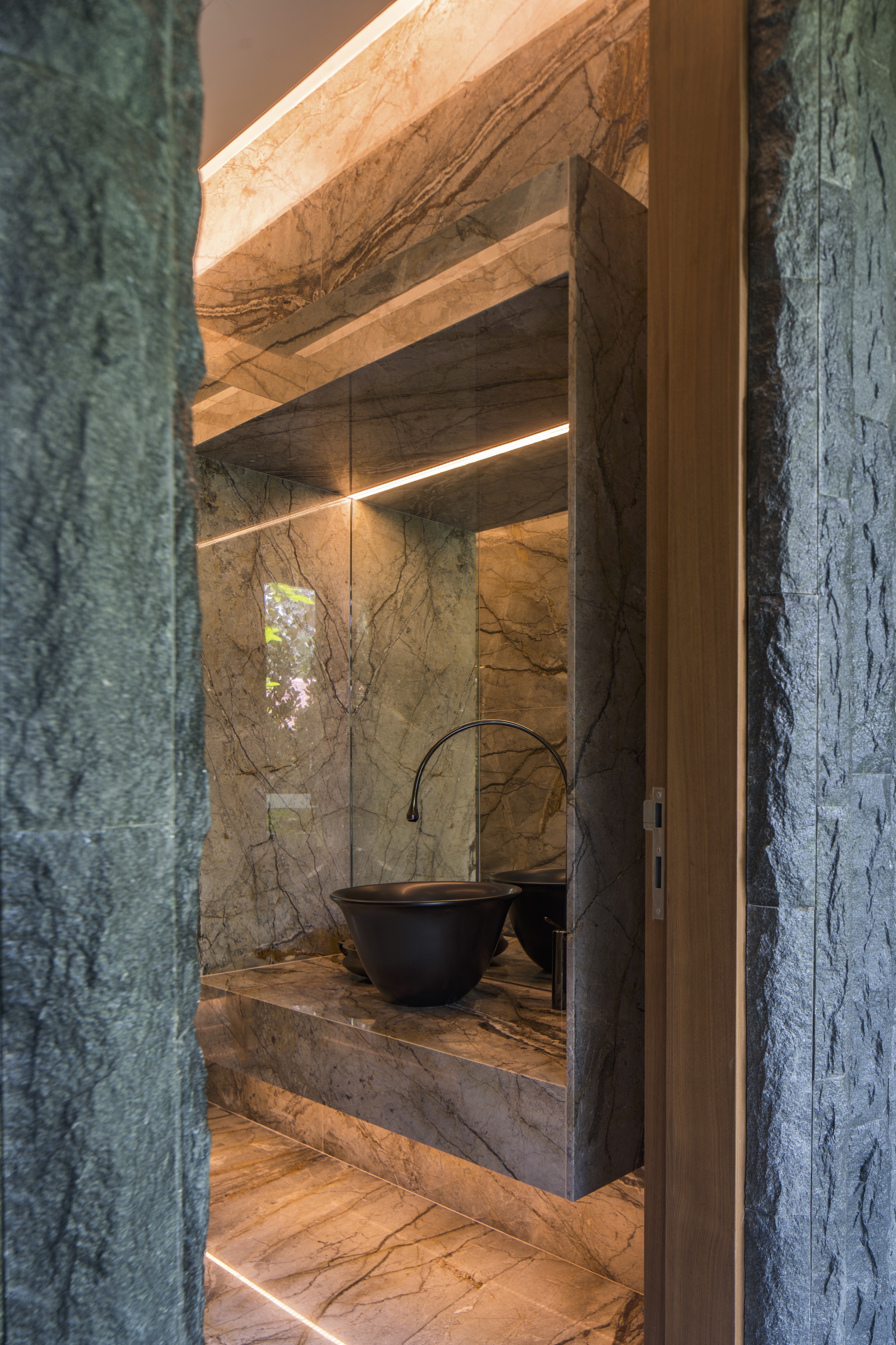 Powder room vanity clad in veined stone with a black vessel sink and backlit mirror