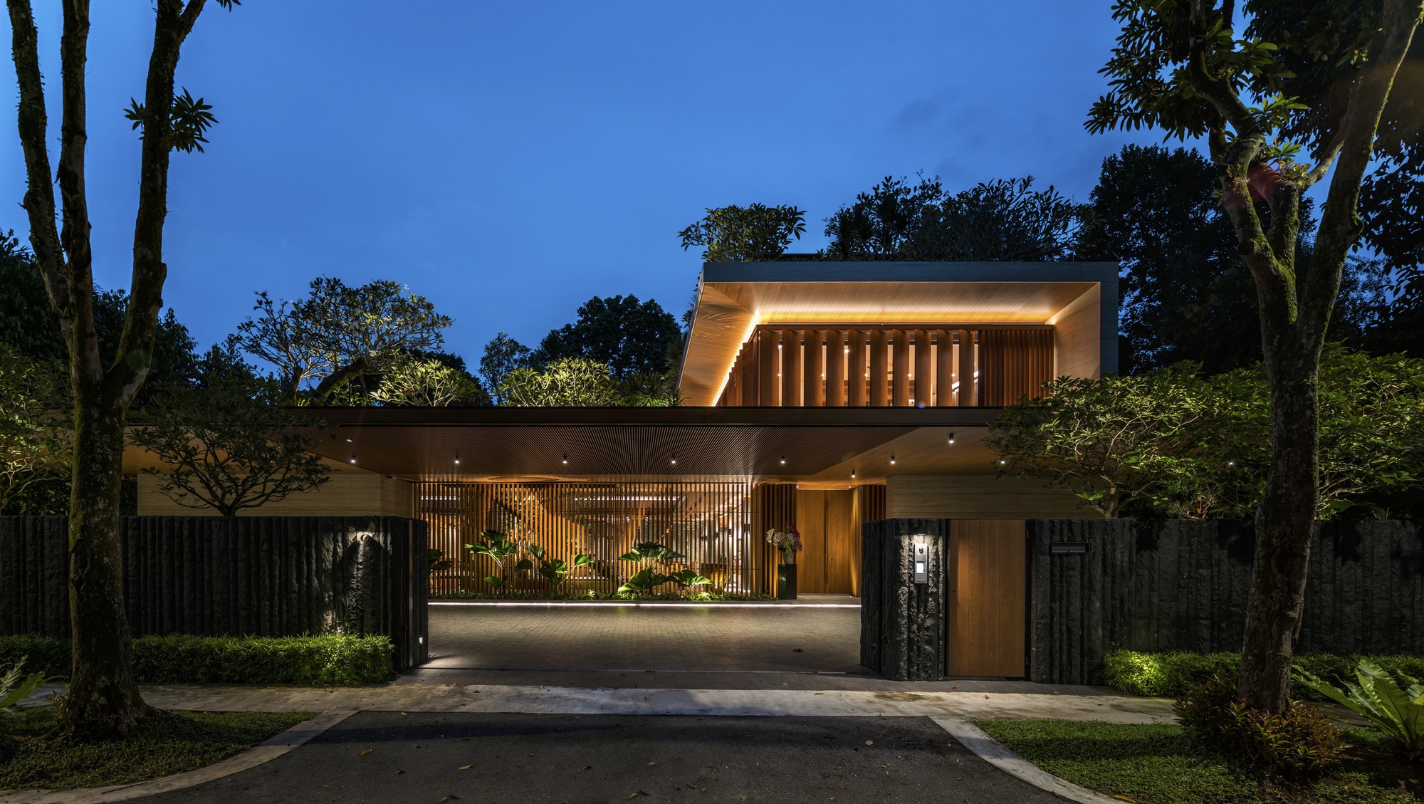 Front elevation with illuminated timber screens and carport at blue hour among surrounding trees