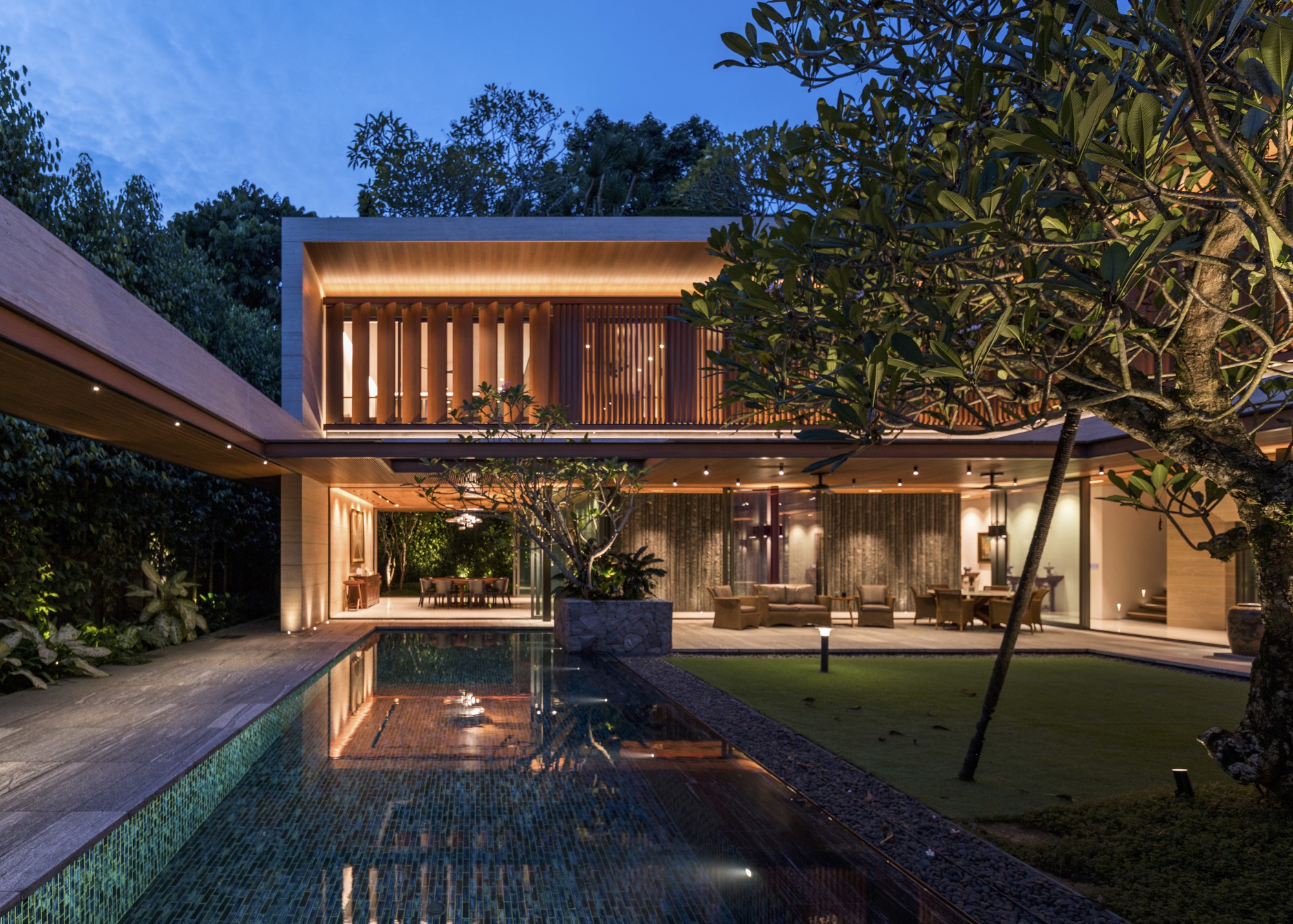 Courtyard pool reflecting the two-story volume with glass walls and uplift timber screens at twilight