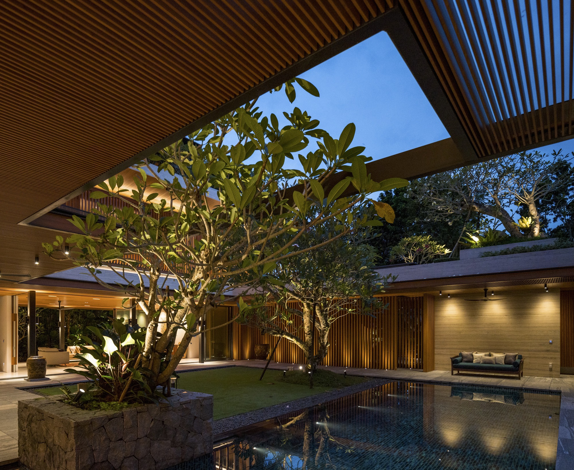 Central courtyard with planted frangipani tree, reflecting pool, and slatted timber ceiling opening to sky